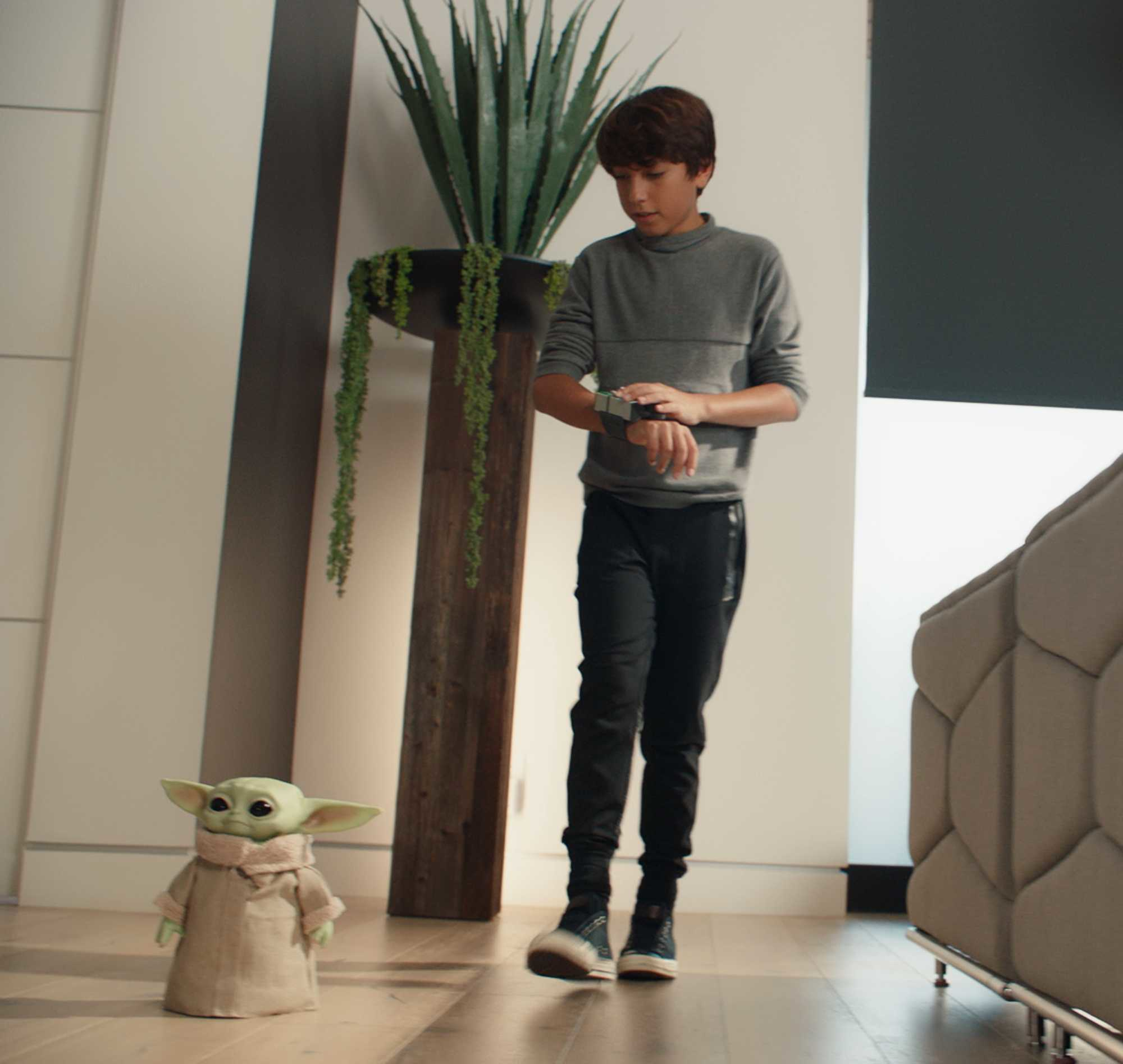 Ein Junge mit Smartwatch und Baby Yoda Spielzeug in einem modernen Wohnzimmer.