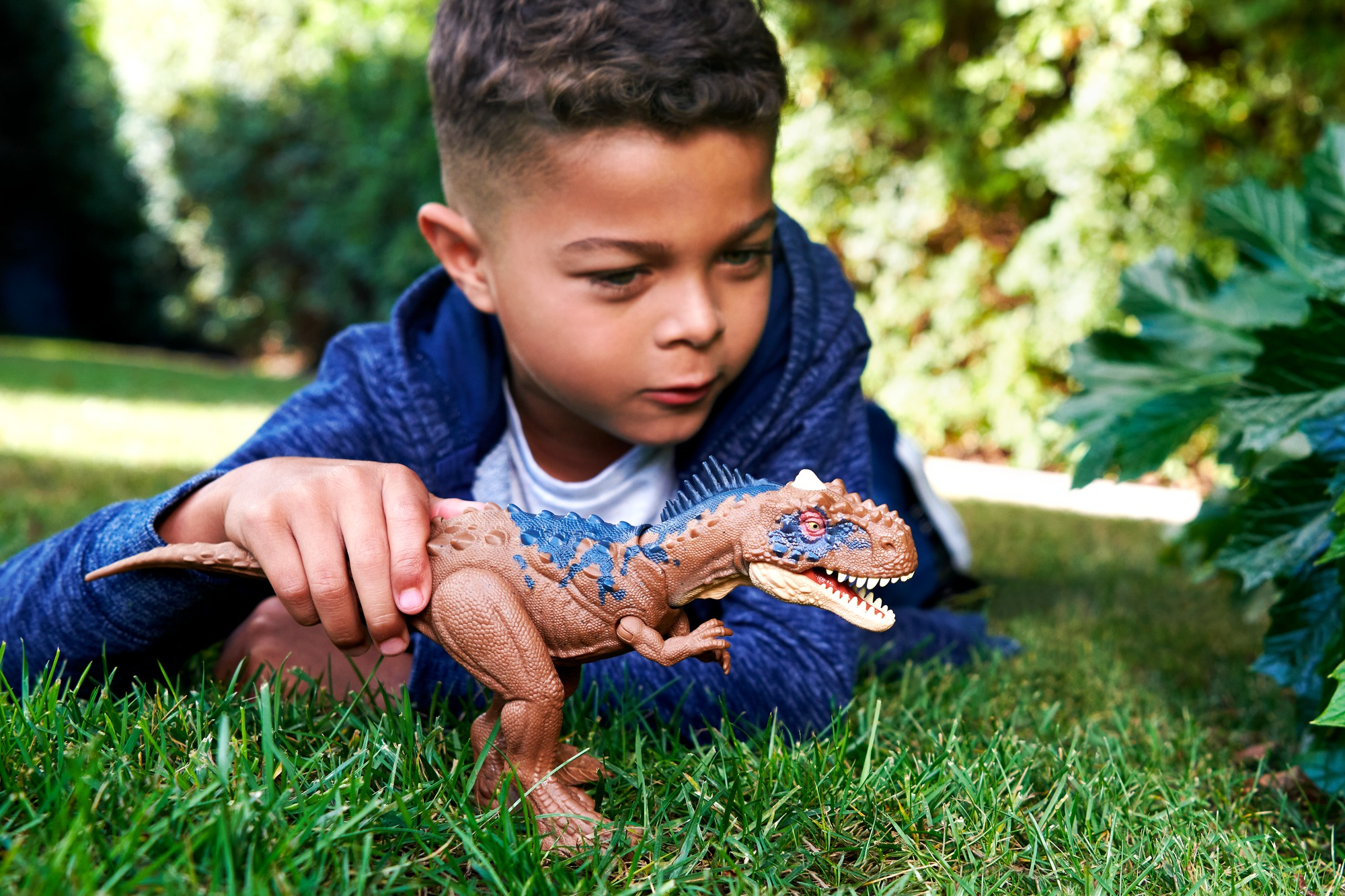 Un ragazzo con un giocattolo di dinosauro sull'erba verde. Il dinosauro è marrone e blu.