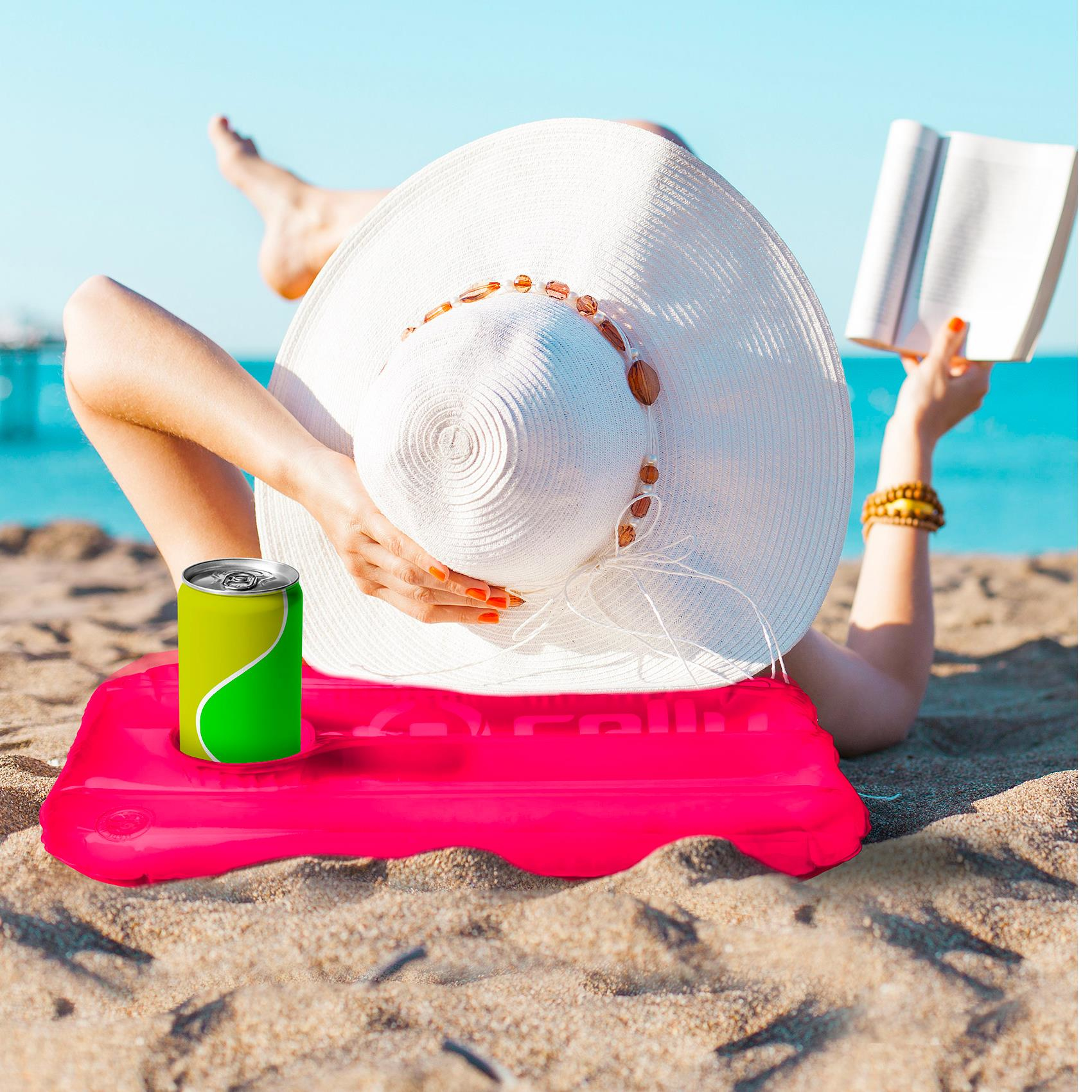 Kobieta na plaży z kapeluszem, książką, różową matą dmuchaną i zieloną puszką po napoju.