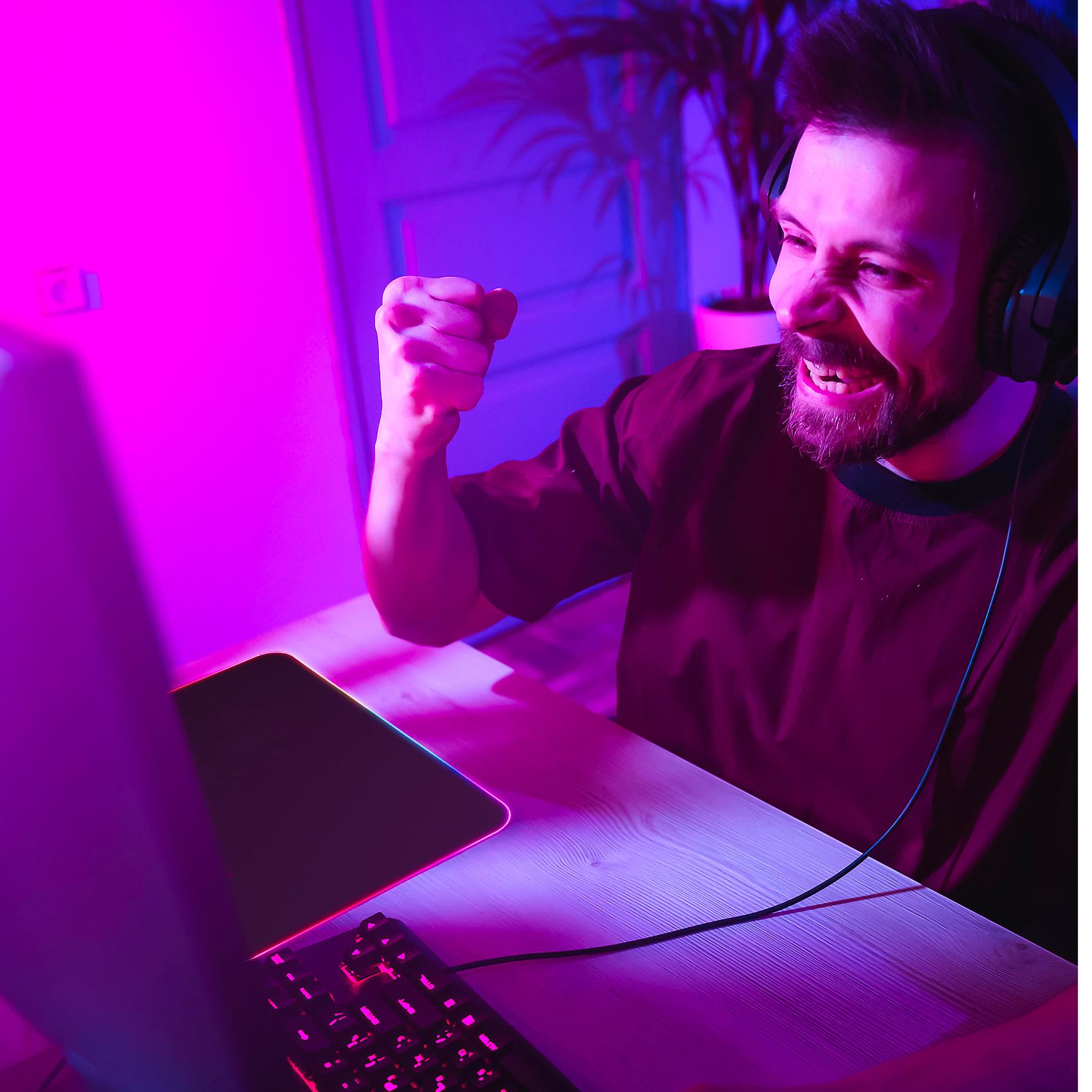 Gracz cieszący się podczas gry, z podświetlaną klawiaturą i podkładką pod mysz w zasięgu wzroku.
