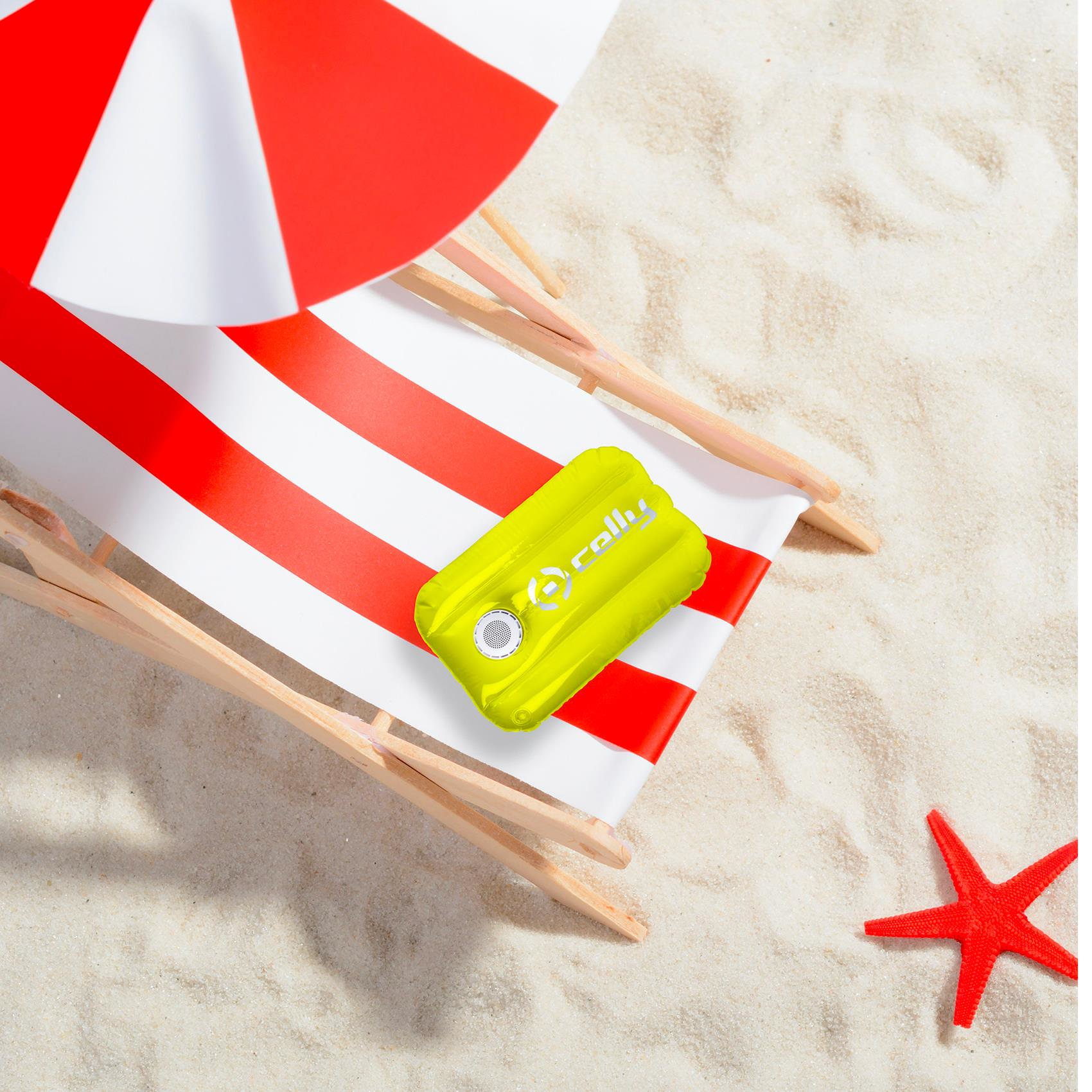 Una scena sulla spiaggia con un altoparlante gonfiabile giallo su una sedia a strisce. Una stella marina rossa è sulla sabbia.