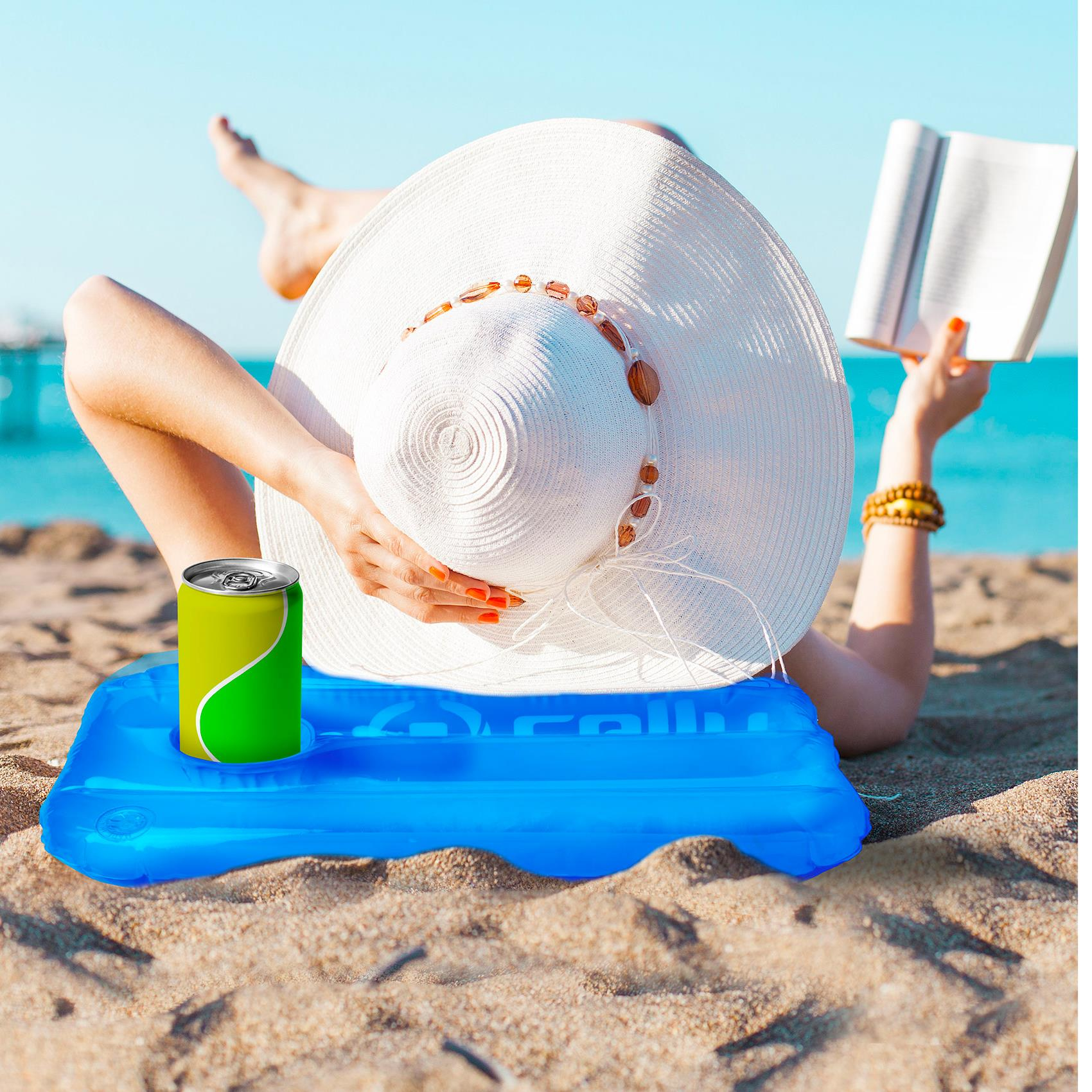 Donna sdraiata su un materassino galleggiante blu con una lattina e un libro sulla spiaggia.