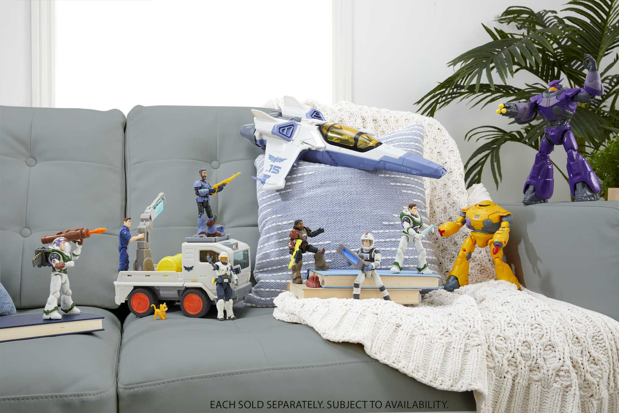 Una scena con varie figure giocattolo su un divano grigio, con una coperta bianca e un cuscino blu.