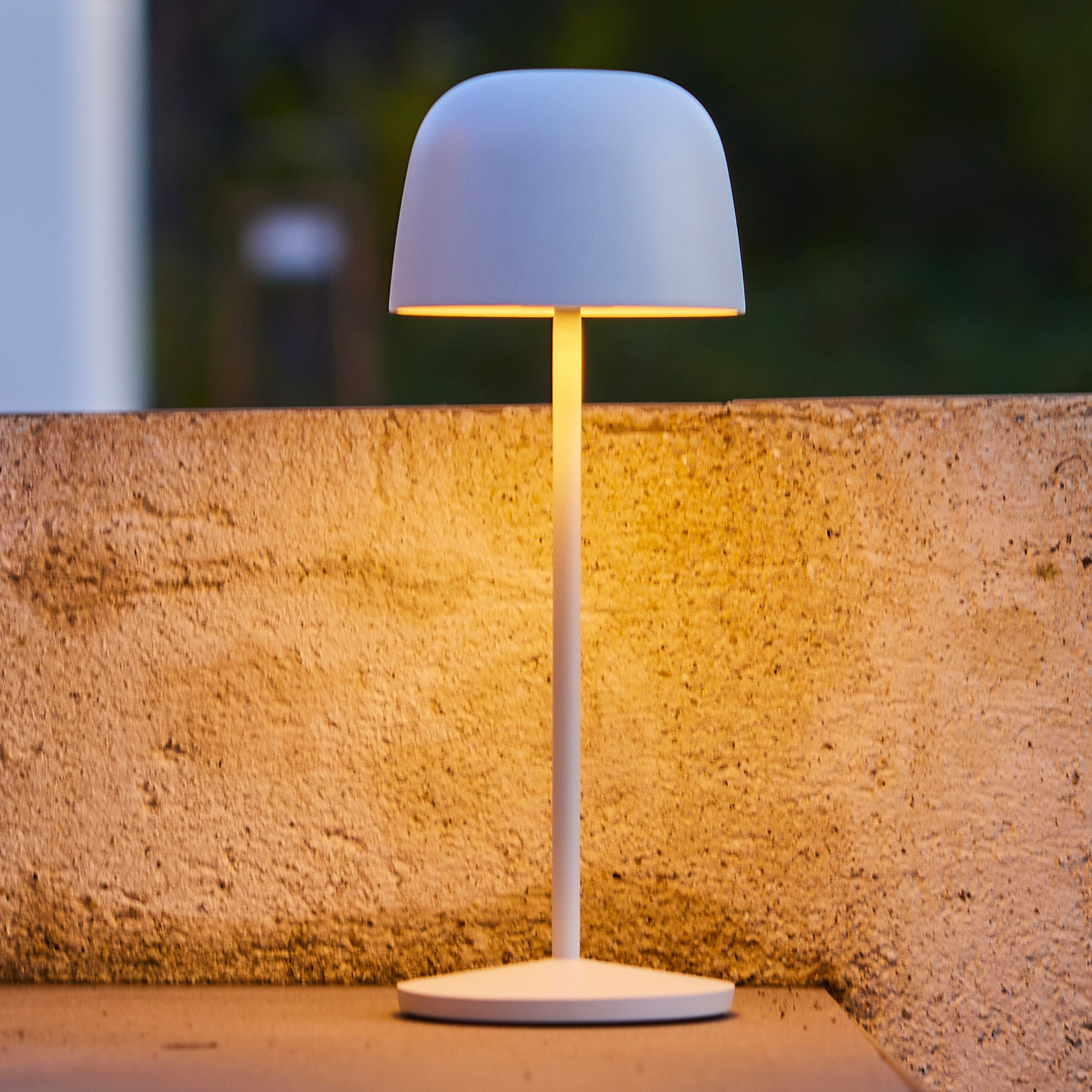 Eine Lampe mit weißem Schirm und Lichtständer. Der Hintergrund ist eine verschwommene Wand.