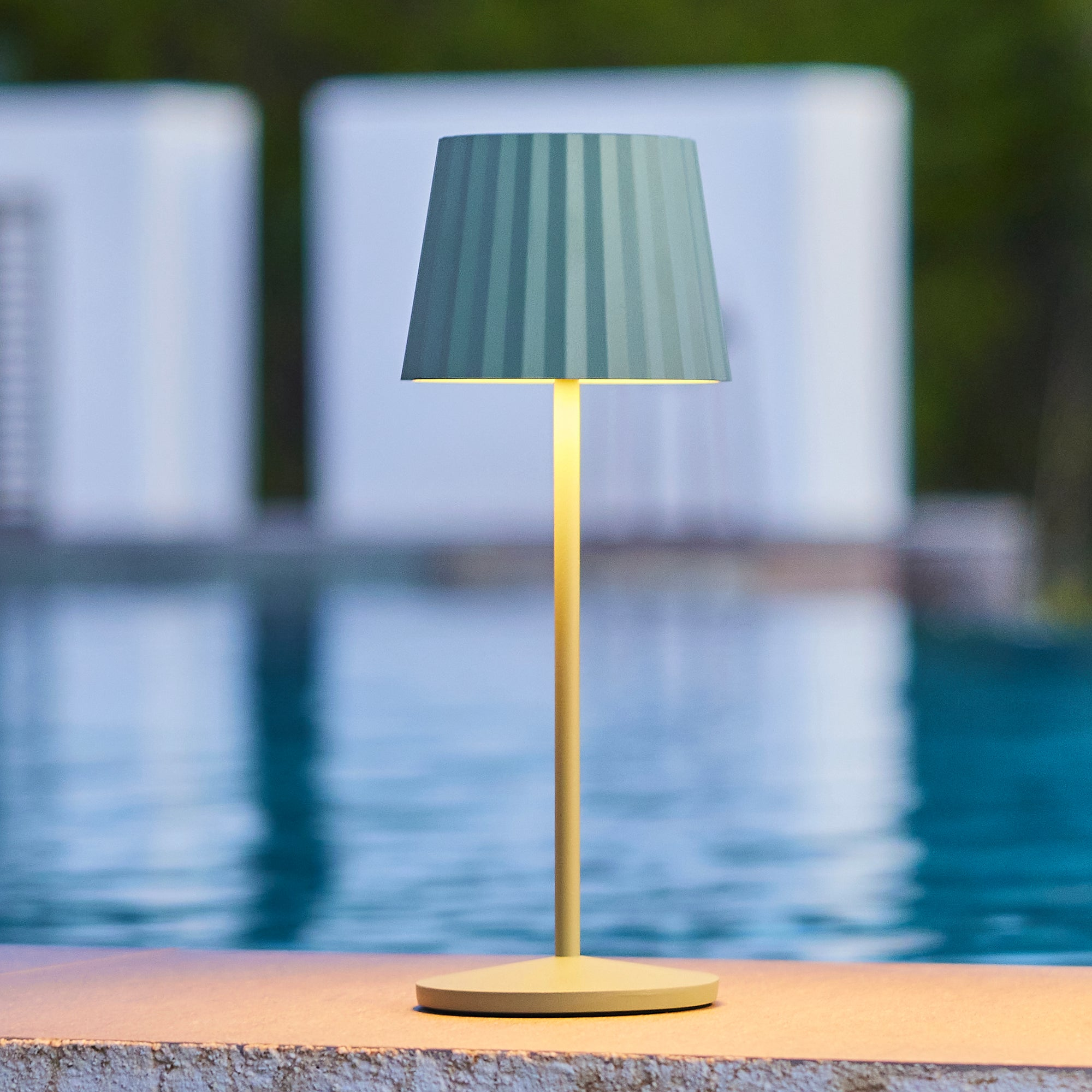 Eine Lampe mit grünem Lampenschirm und Lichtständer. Der Hintergrund ist ein Pool.