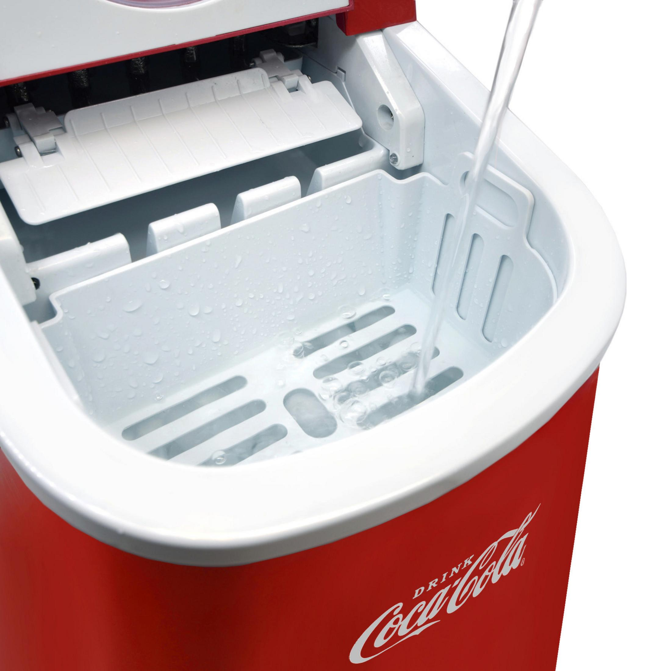 La parte superiore aperta di una macchina per il ghiaccio Coca-Cola rossa con acqua che vi si versa dentro.