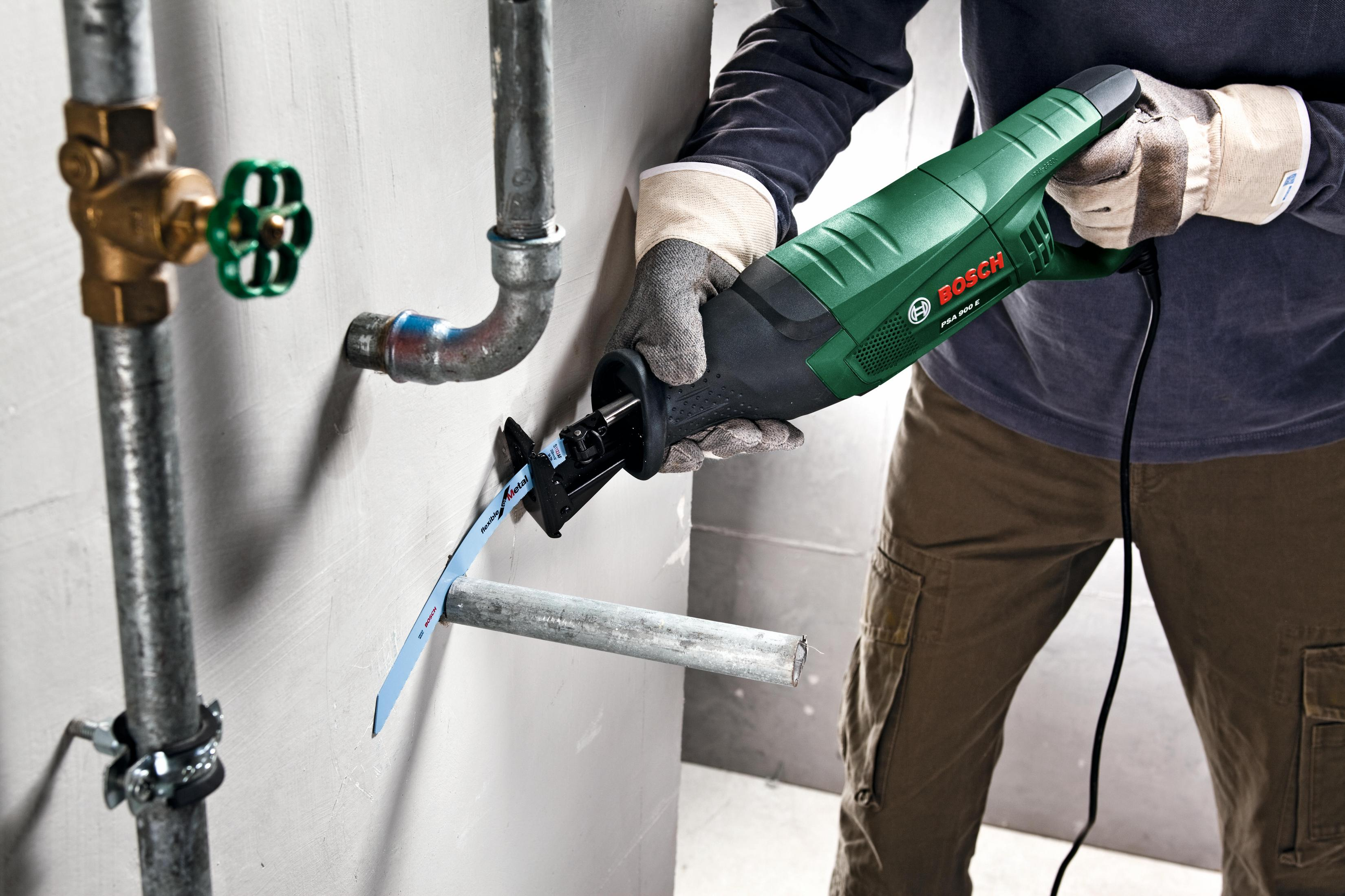Osoba używa zielono-czarnej piły do przecięcia metalowej rury.