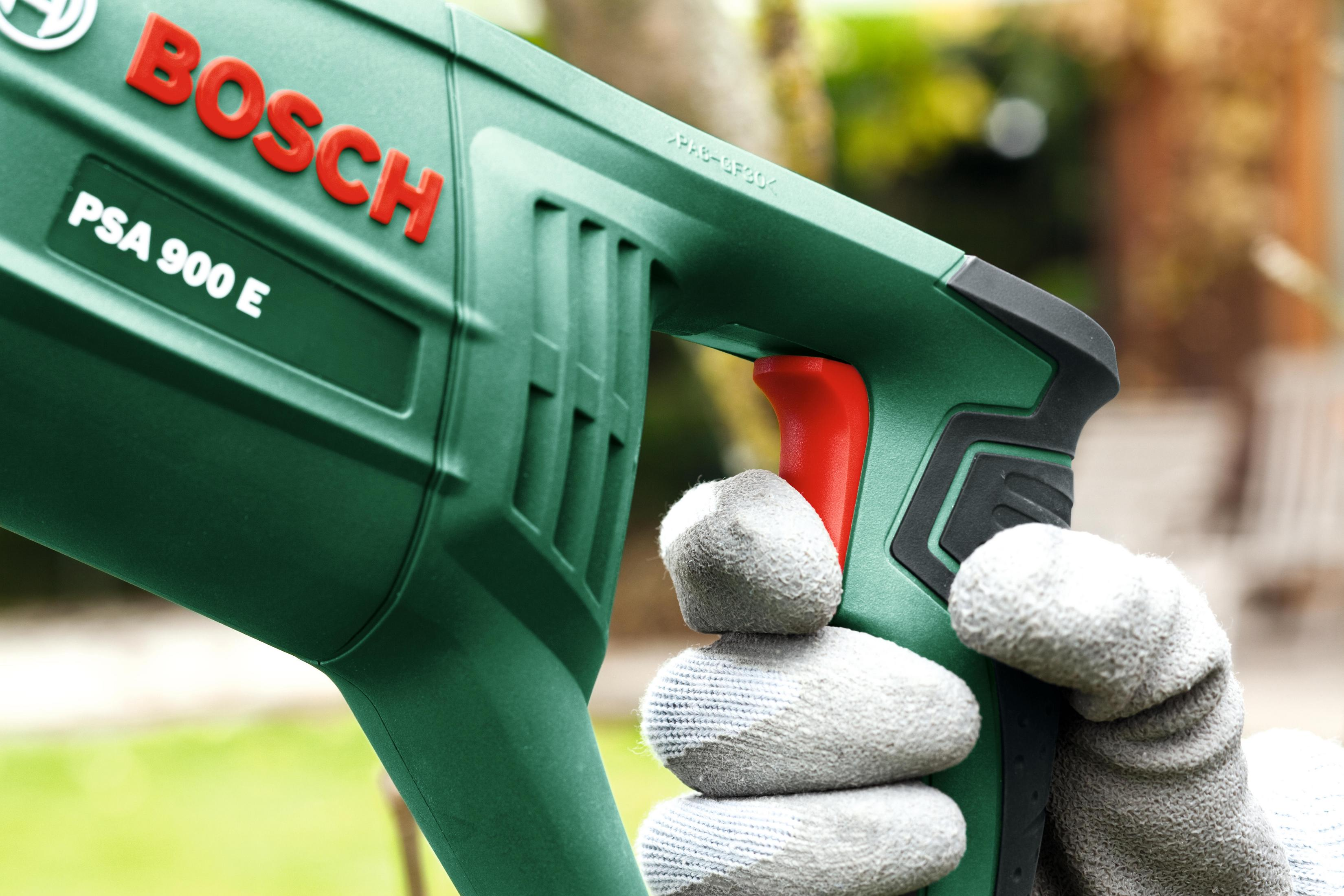 Ręka osoby w rękawicy trzyma zieloną piłę ze słowem BOSCH.