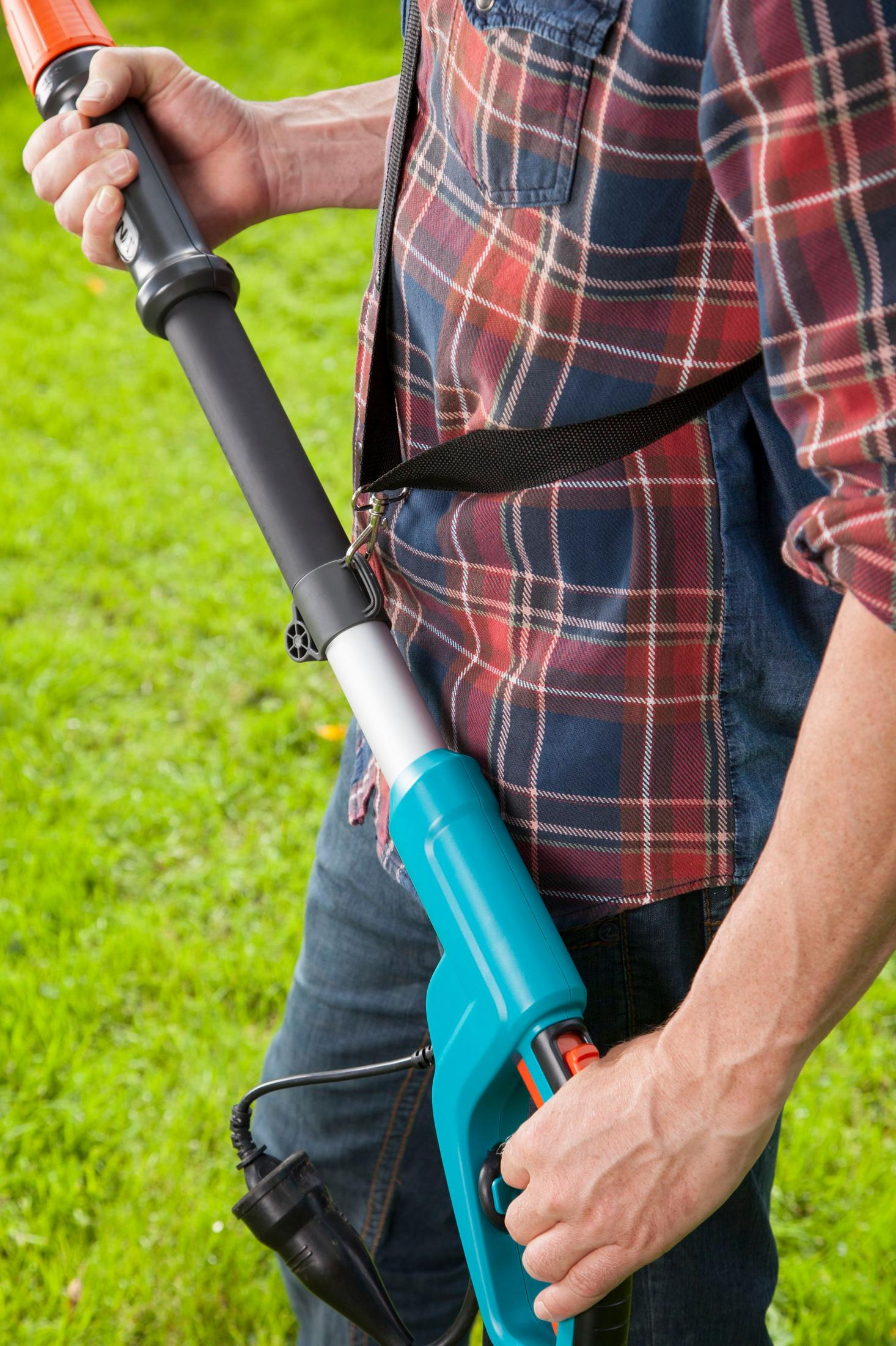 Uomo che tiene un lungo attrezzo Gardena, con un prato verde sullo sfondo.