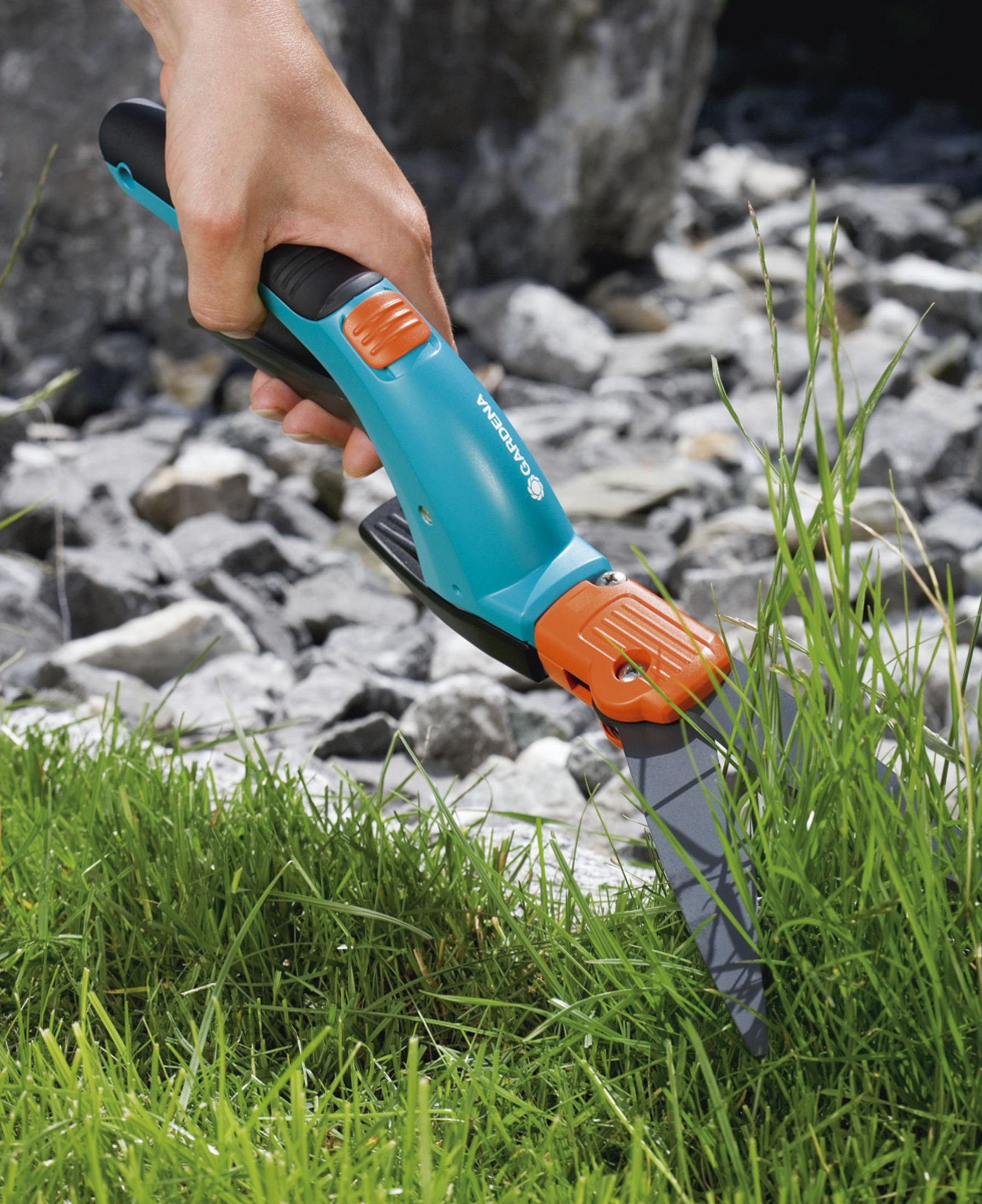 Eine Person schneidet Gras mit einem blau-orangenen manuellen Trimmer.