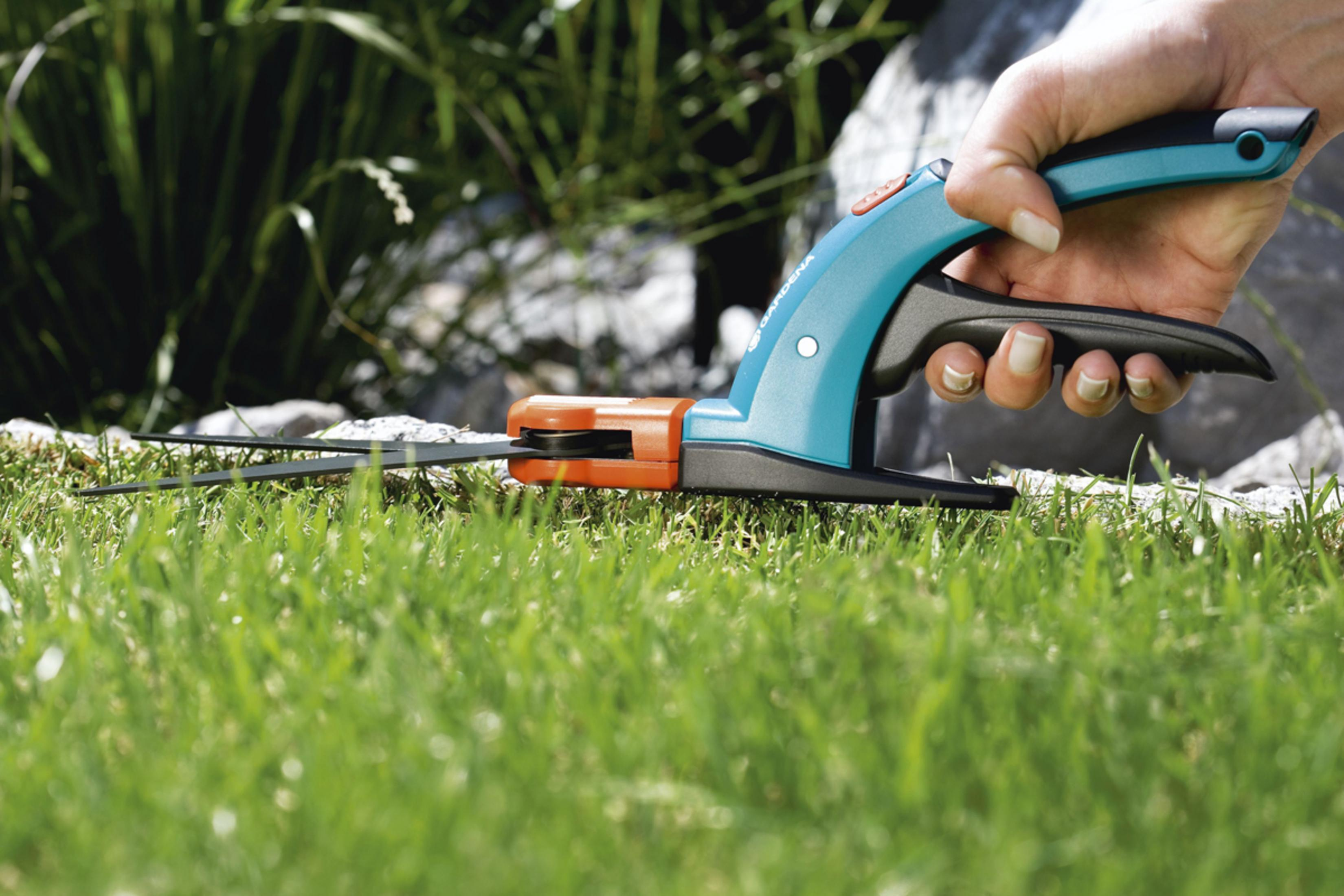 Eine Person schneidet Gras mit einem blau-orangenen manuellen Trimmer.
