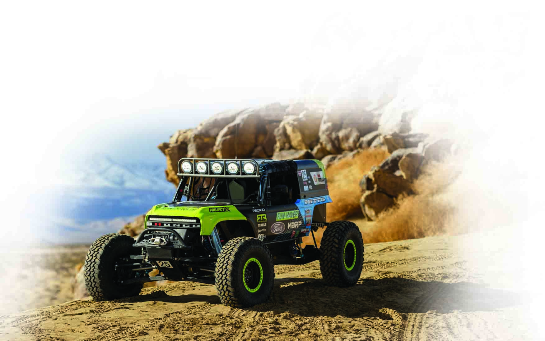 Offroad-Rennwagen auf einer Dirt-Strecke. Gelbe, grüne und schwarze Farben. Felsiger Hintergrund mit hellem Himmel.