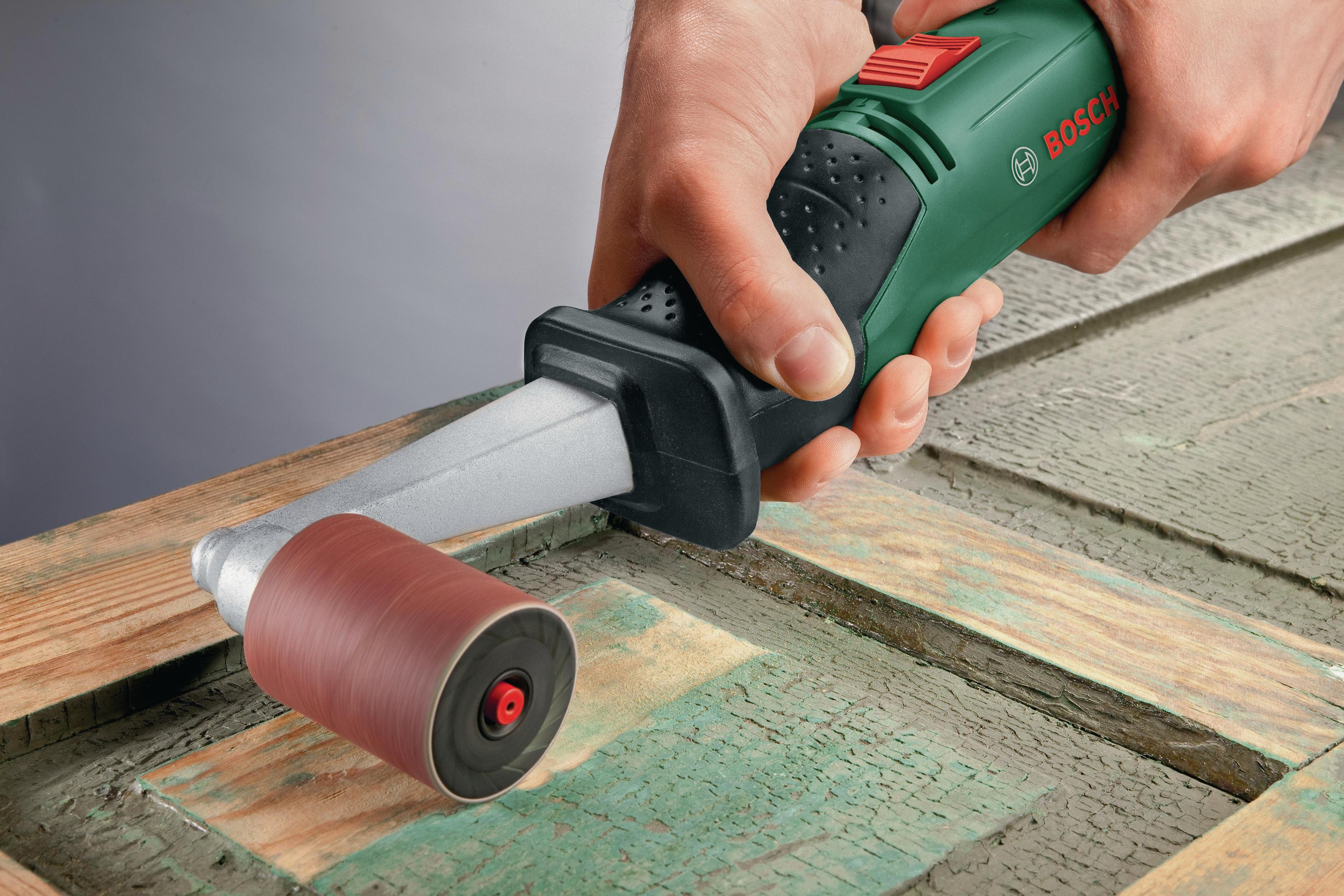 Mężczyzna szlifujący drewno elektronarzędziem Bosch. Zielono-czarne narzędzie. Drewniana powierzchnia. Ręka na narzędziu.