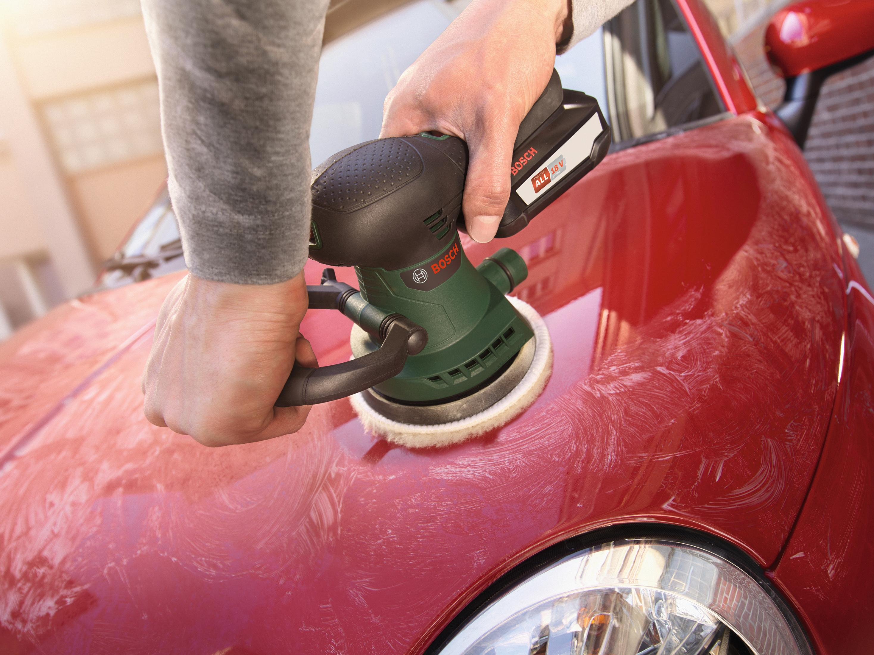 Une main utilisant une polisseuse Bosch sur le capot d'une voiture rouge pour enlever les tourbillons et les rayures.
