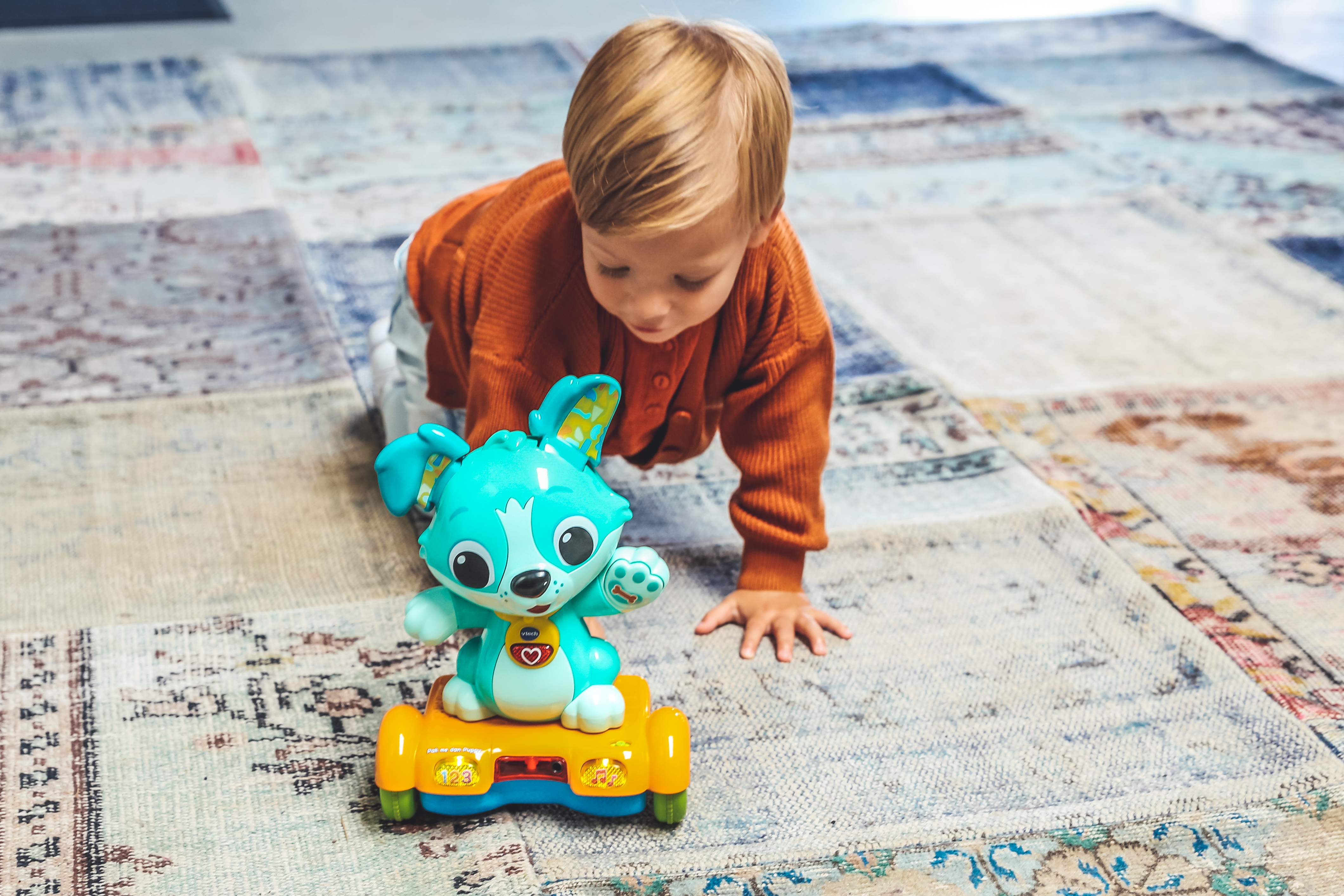 Ein Kleinkind spielt mit einem Spielzeug-Hasen auf einem gemusterten Teppich.