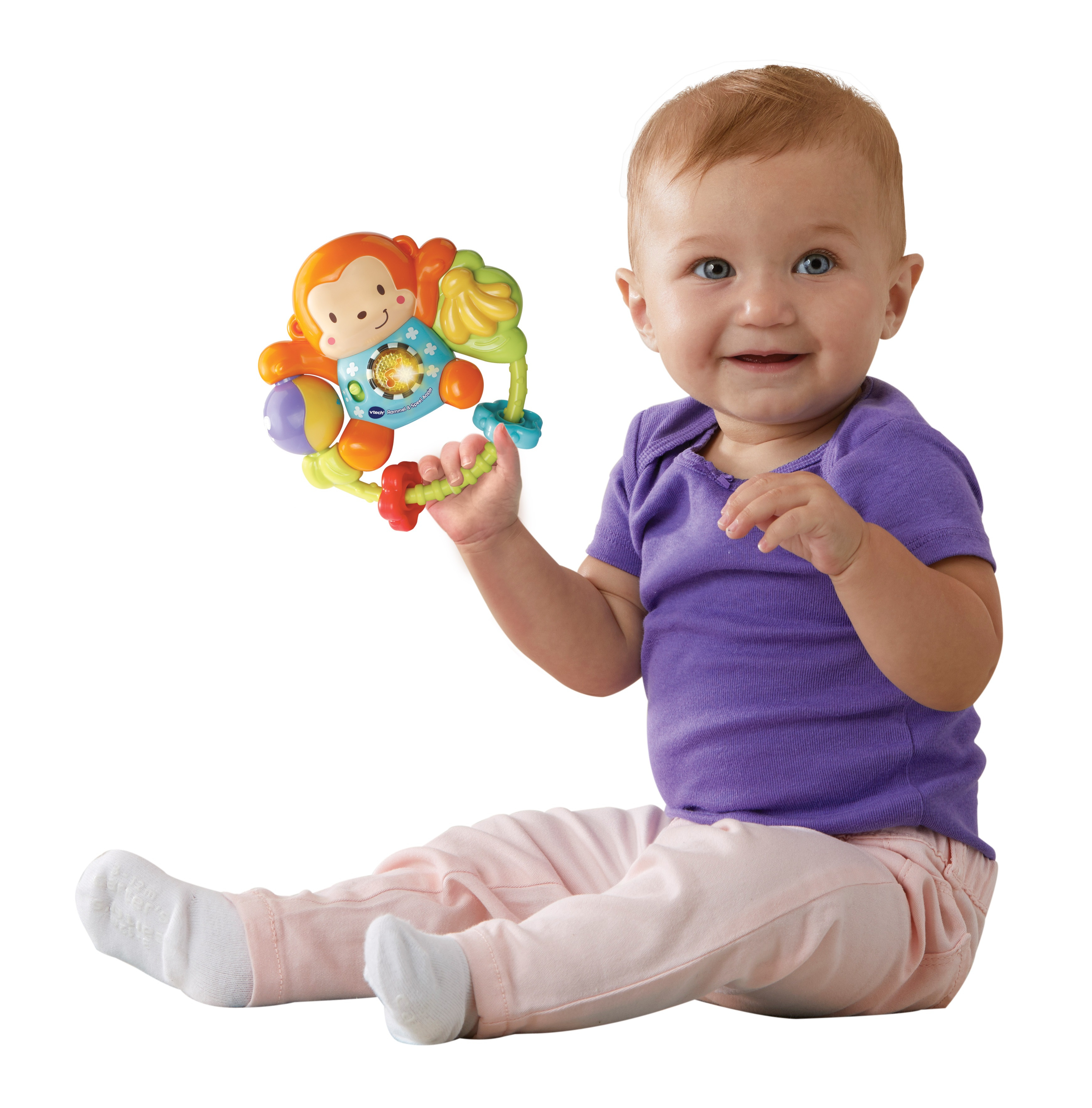Ein Baby hält ein buntes Spielzeug mit einem Affen, sitzt auf dem Boden und lächelt.