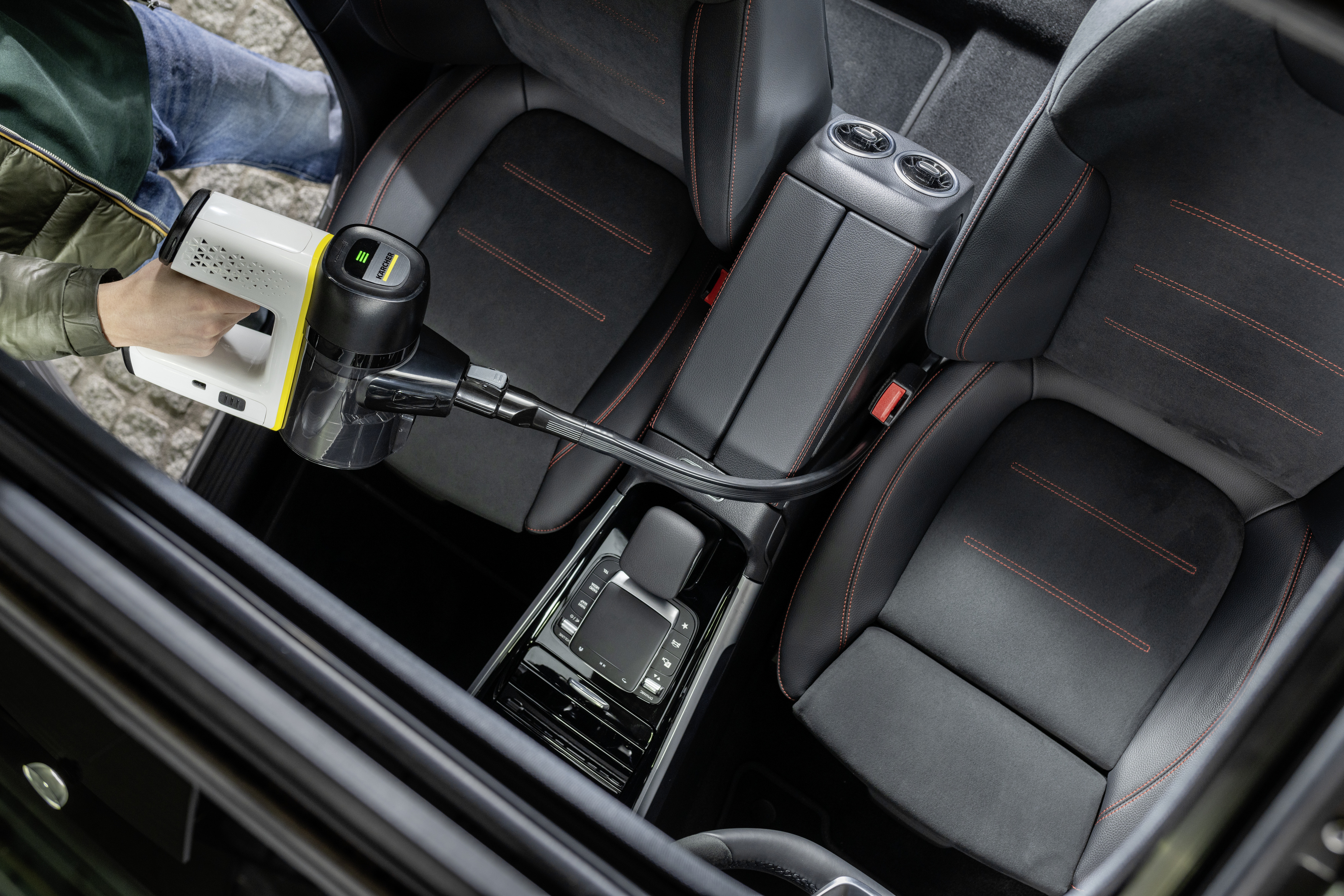 A person vacuums a car interior with a handheld vacuum cleaner. The car seats are black.