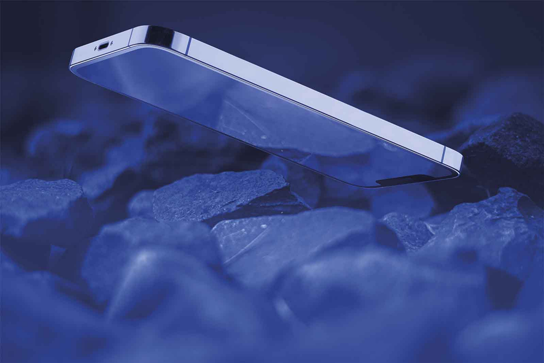 Uno smartphone argentato sospeso sopra rocce blu scuro, con uno sfondo sfocato.
