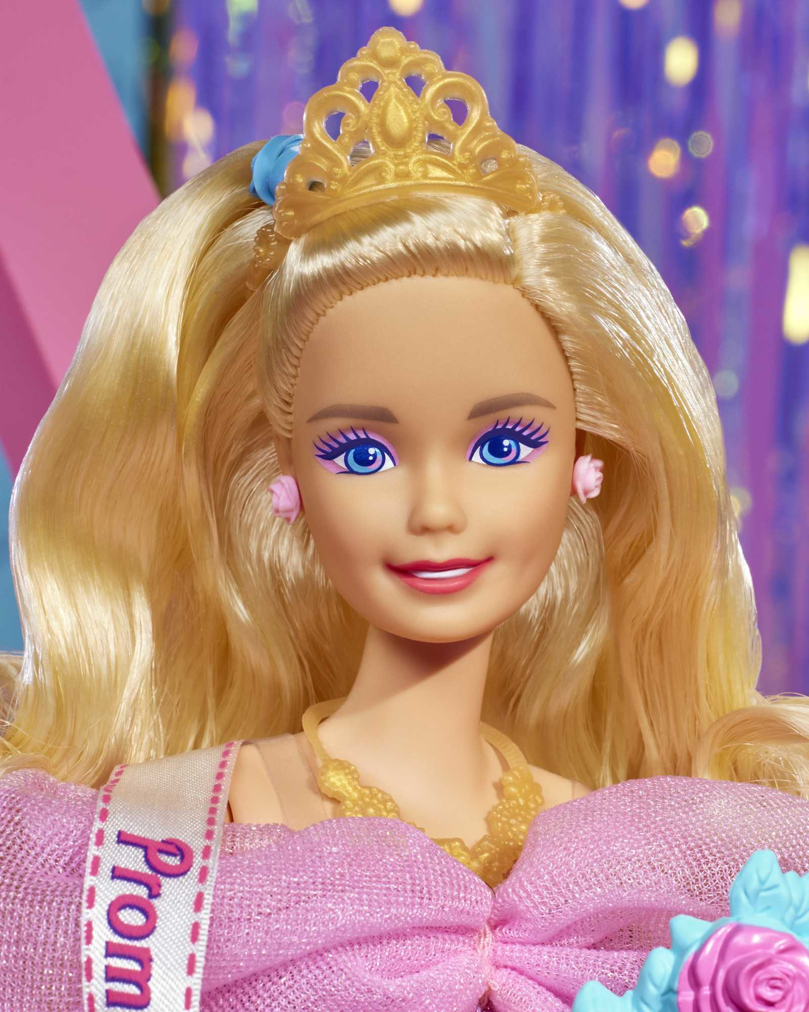 Primer plano de muñeca Barbie con pelo rubio, tiara y vestido rosa, fondo borroso.