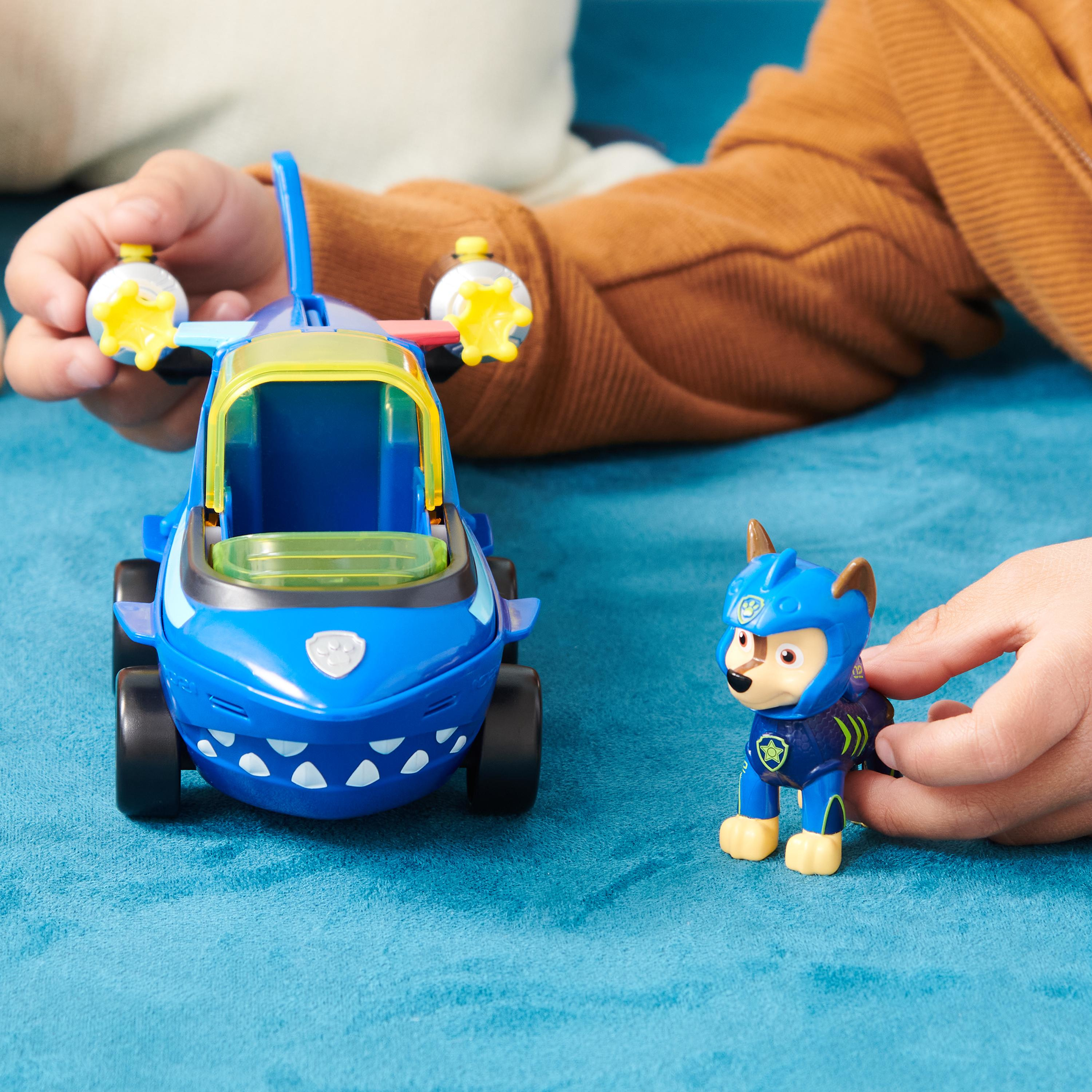 Kinderhände spielen mit einem blauen Spielzeugflugzeug und einer Paw Patrol Chase-Figur auf blauer Oberfläche.
