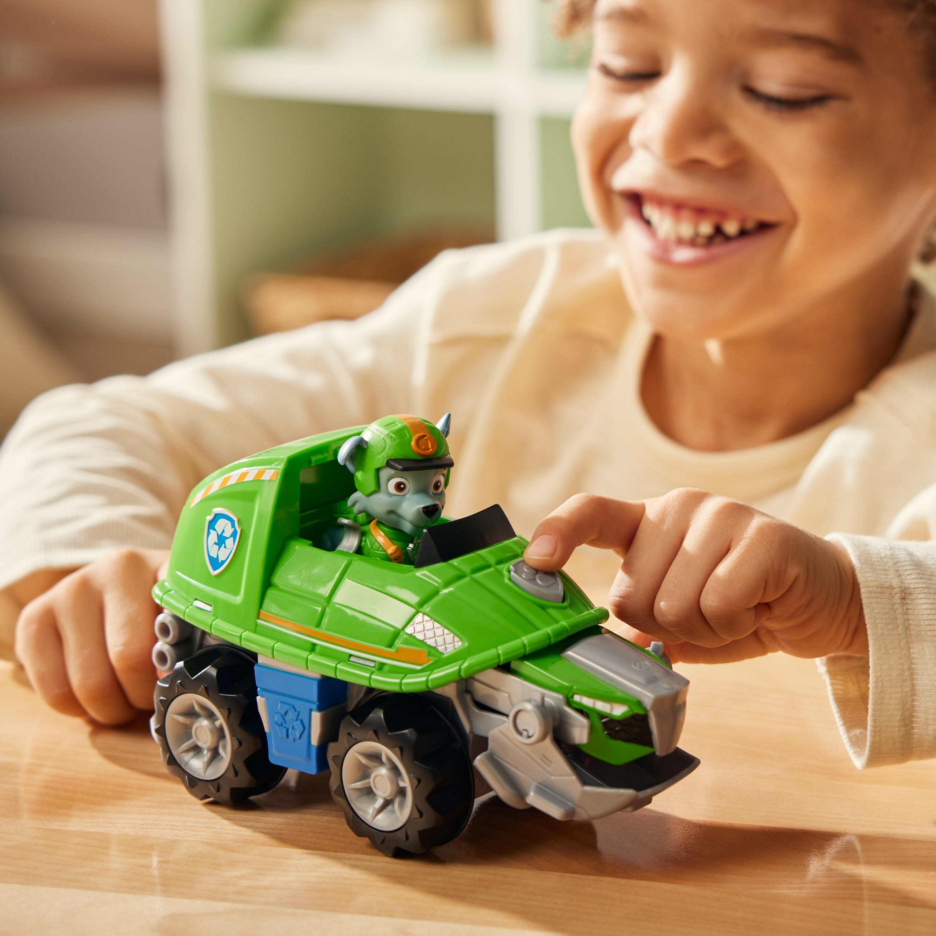 Ein Junge spielt mit einem grünen Paw Patrol-Truck-Spielzeug. Der Truck hat eine Hundefigur auf dem Fahrersitz.