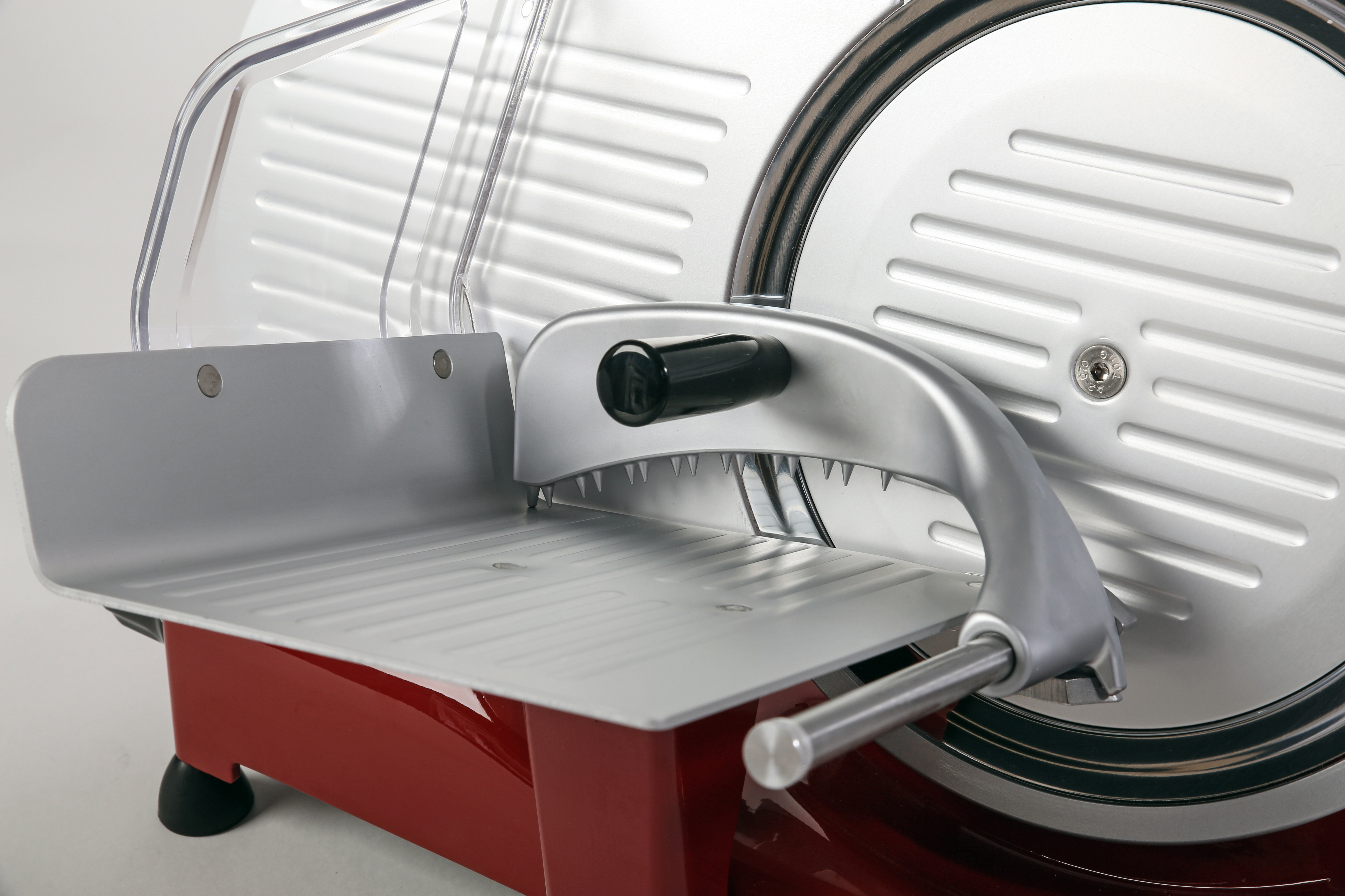 Czerwona i srebrna krajalnica do mięsa na białym tle. Posiada przezroczystą osłonę.