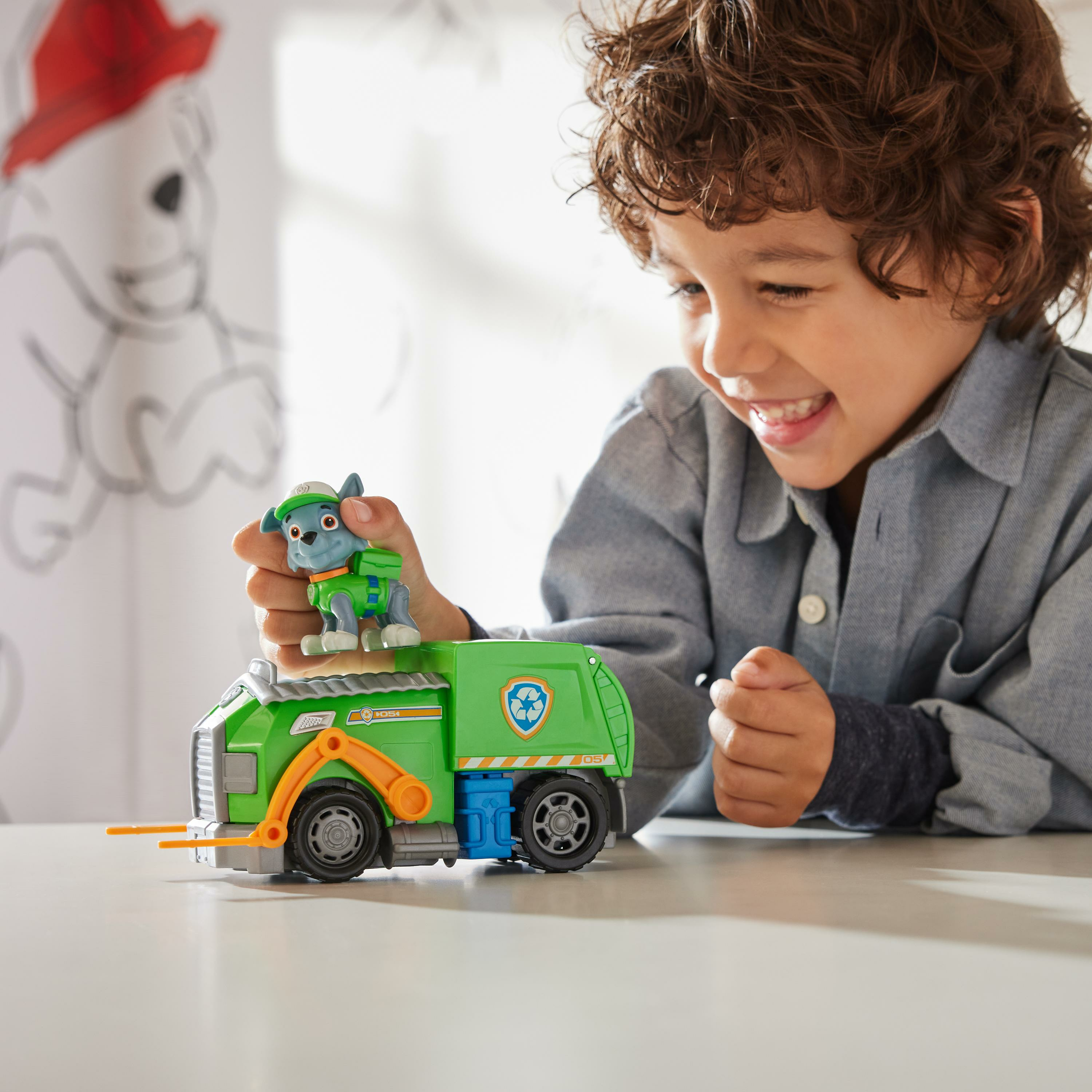 Ein Junge spielt mit einem grünen Müllwagen-Spielzeug und einer Hundefigur.