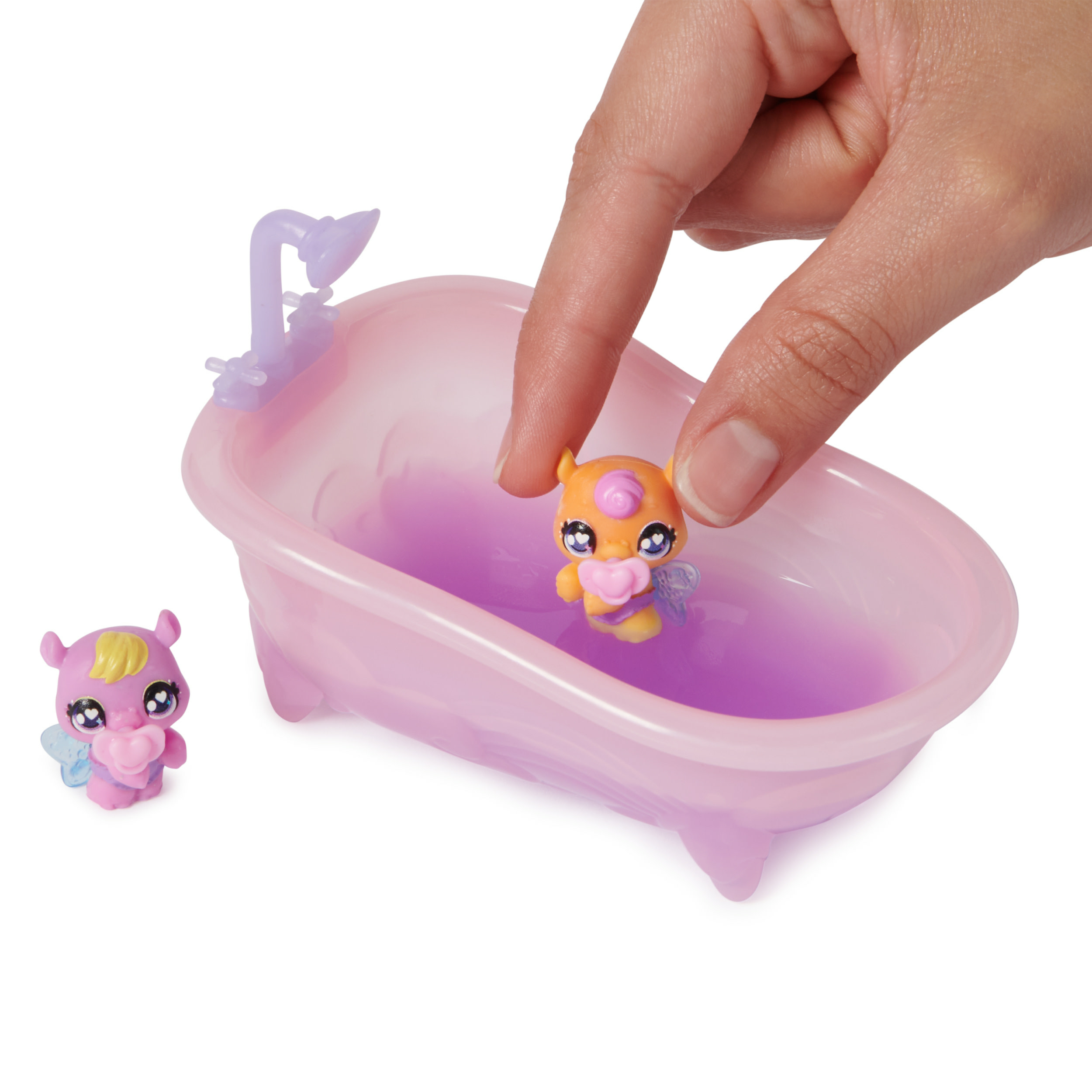 Eine Hand hält eine Spielzeugfee in einer rosa Badewanne mit lila Wasser.
