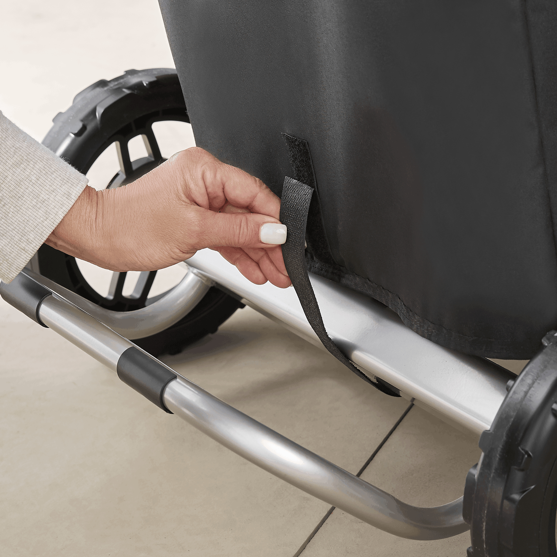 Ręka reguluje czarny pasek na czarno-srebrnym wózku.