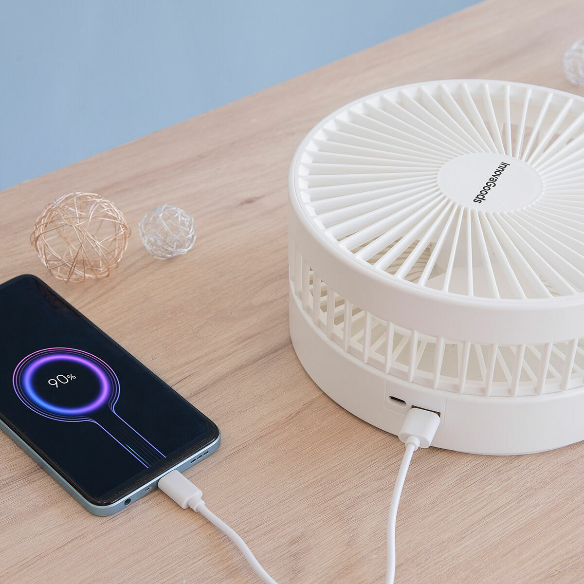Un teléfono cargándose con un ventilador blanco al lado.