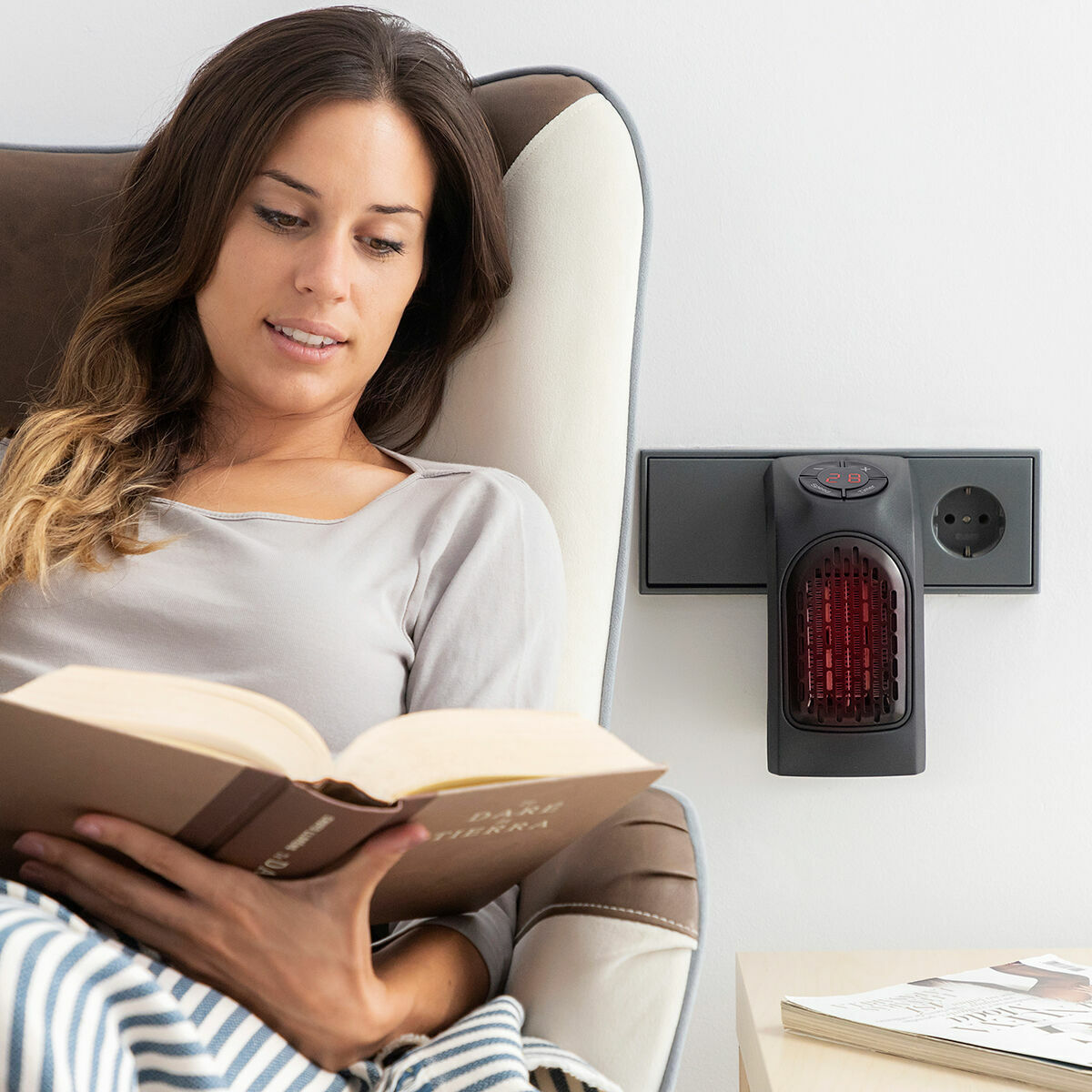 Una mujer leyendo un libro cerca de un calefactor de pared.