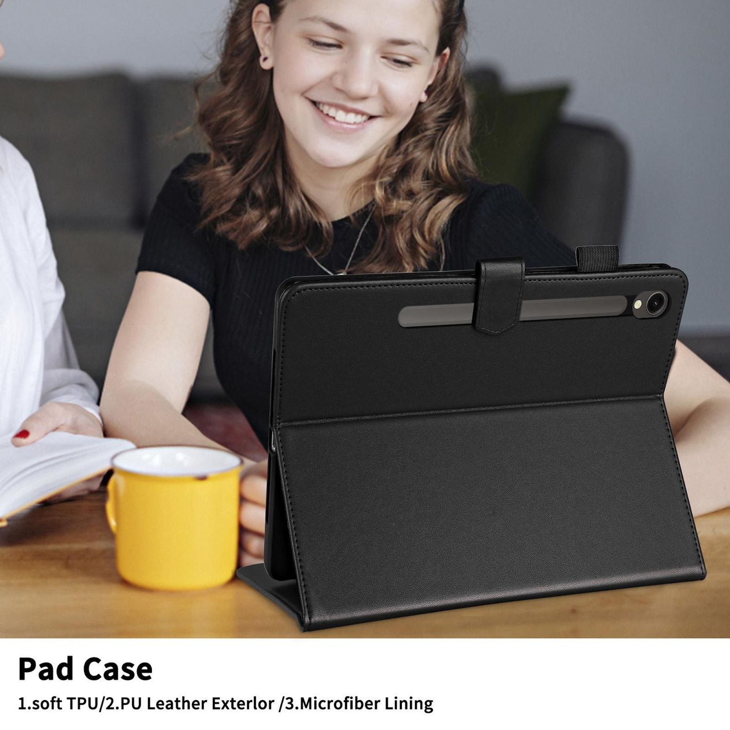 Una mujer sonríe mientras usa una funda negra para tableta. Una taza amarilla está sobre una mesa.