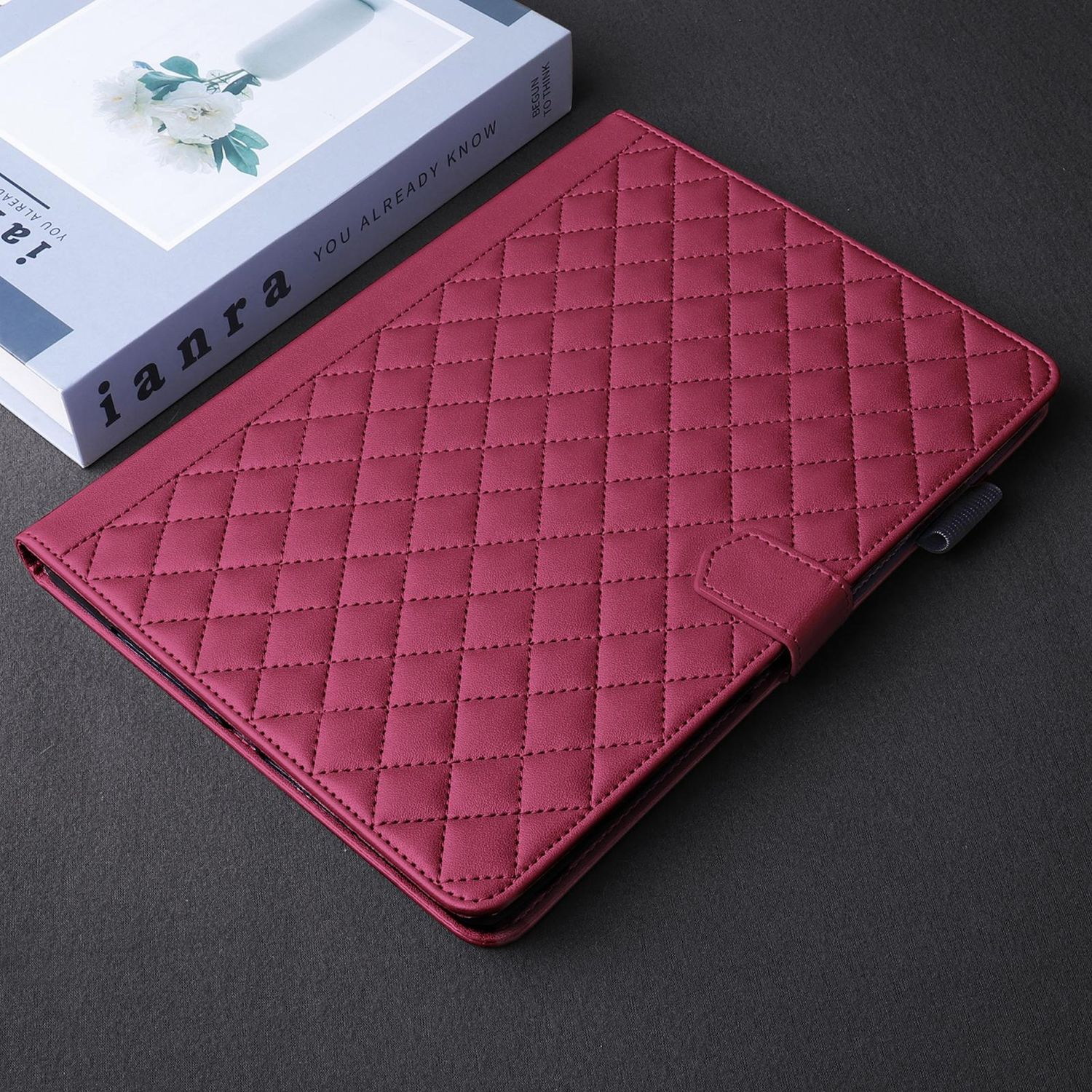 Funda de tableta granate con costuras de diamante, ranura para bolígrafo y cierre. Un libro en el fondo.
