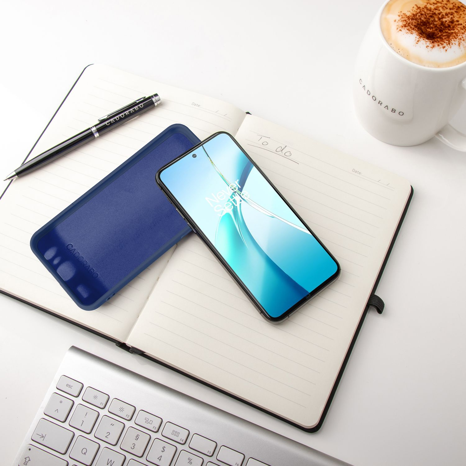 Telefon, Handyhülle, Stift und Tasse auf einem Notizblock, Tastatur im Hintergrund.