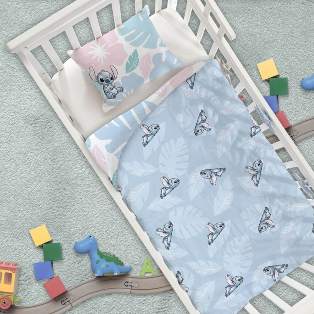 Kinderbett mit Stitch-Bettwäsche: Kissen, Decke und Spielzeug auf dem Boden.