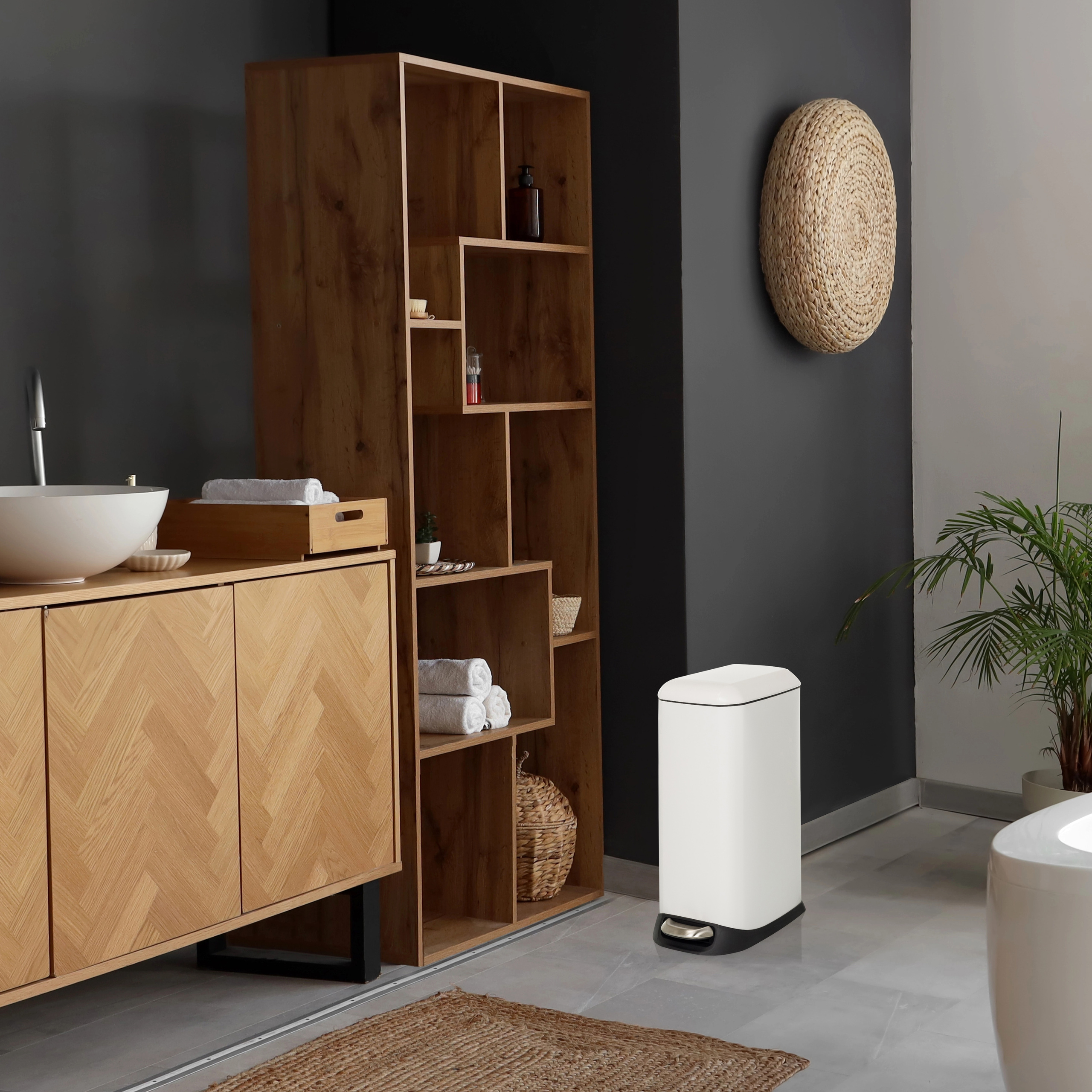Ein modernes Badezimmer mit Holzschrank, hohem Regal und weißem Mülleimer.