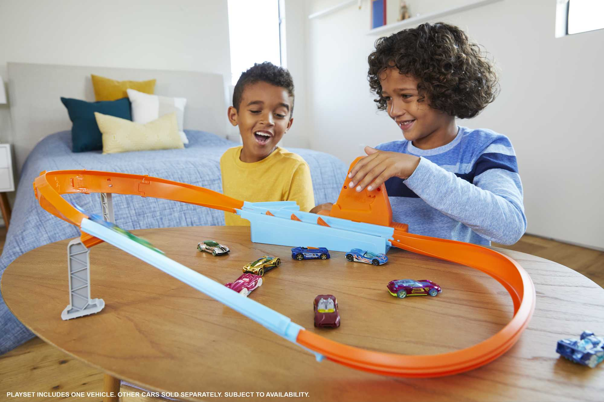 Zwei Jungen spielen mit einer Hot Wheels-Bahn. Die Strecke ist orange und blau, mit Autos darauf.