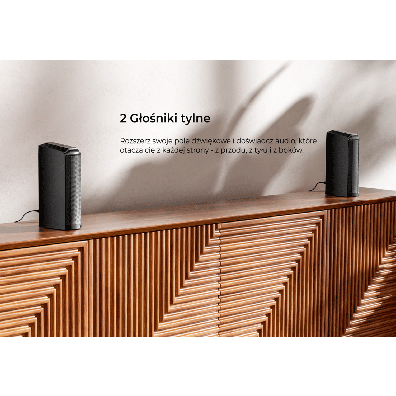 Dwa czarne głośniki na drewnianej szafce. Tekst o głośnikach znajduje się nad szafką.