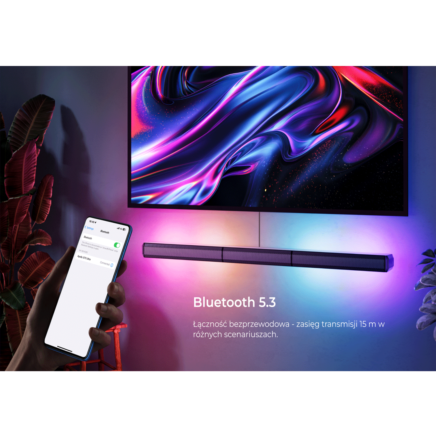 Telewizor z abstrakcyjną grafiką, soundbar poniżej, telefon w dłoni.