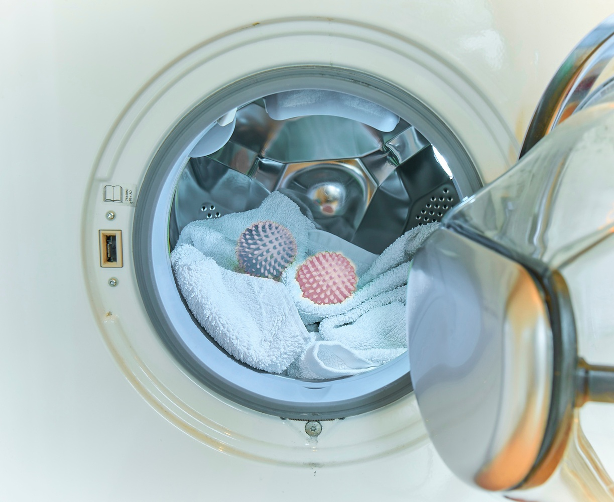 Pralka z białym ręcznikiem i dwiema kulkami do suszarki w środku.
