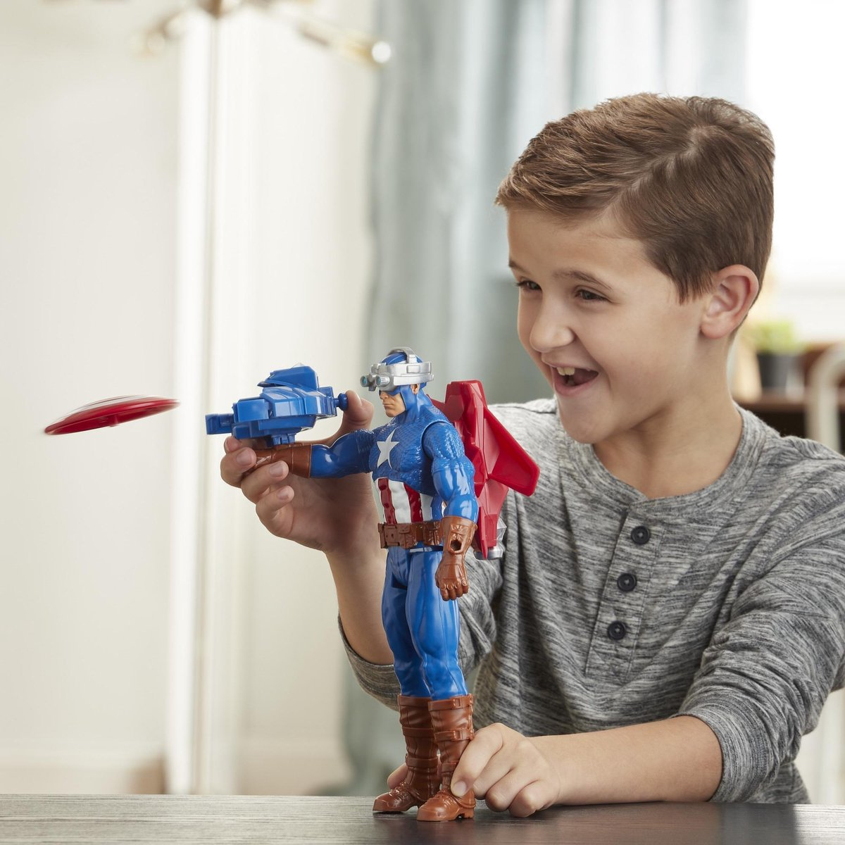 Un bambino gioca con un giocattolo di Capitan America. Sorride mentre tiene la figura e punta uno scudo.