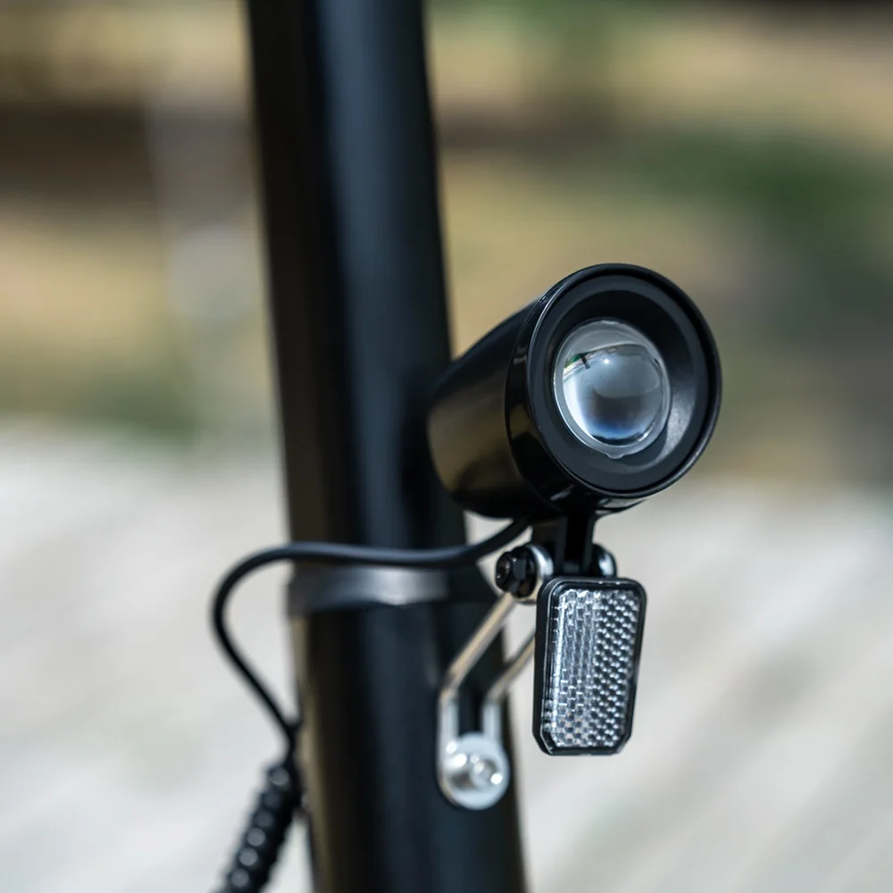 Primo piano del faro dello scooter elettrico. Nero, rotondo, con lente trasparente. Sfondo sfocato.