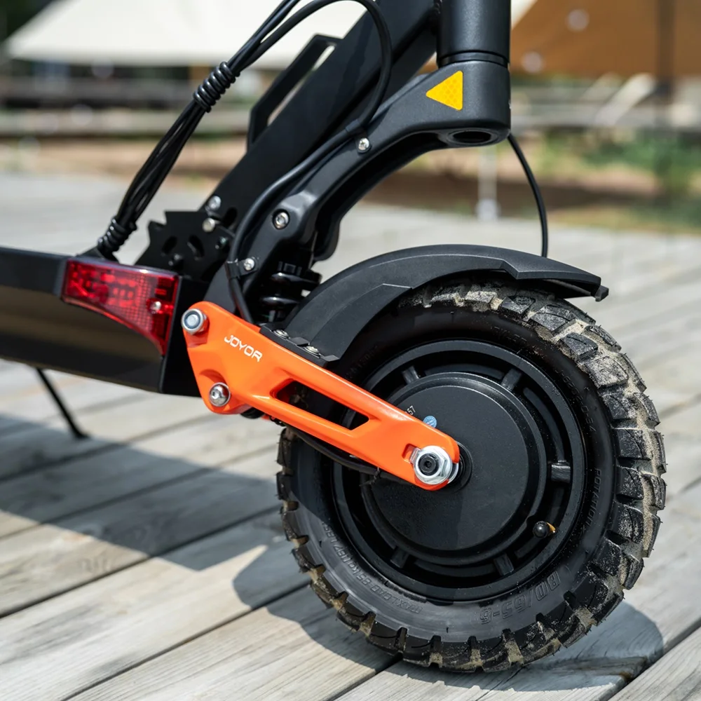 Primo piano del pneumatico e dei dettagli delle sospensioni di uno scooter elettrico. Colori arancione, nero e grigio.