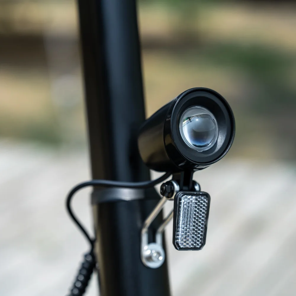 Primo piano del faro nero di uno scooter elettrico con un riflettore, su uno sfondo sfocato.