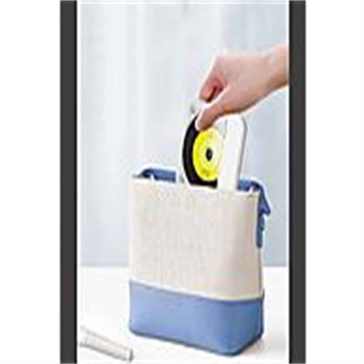 Eine Hand, die eine gelbe Scheibe in eine blau-weiße Tasche legt.