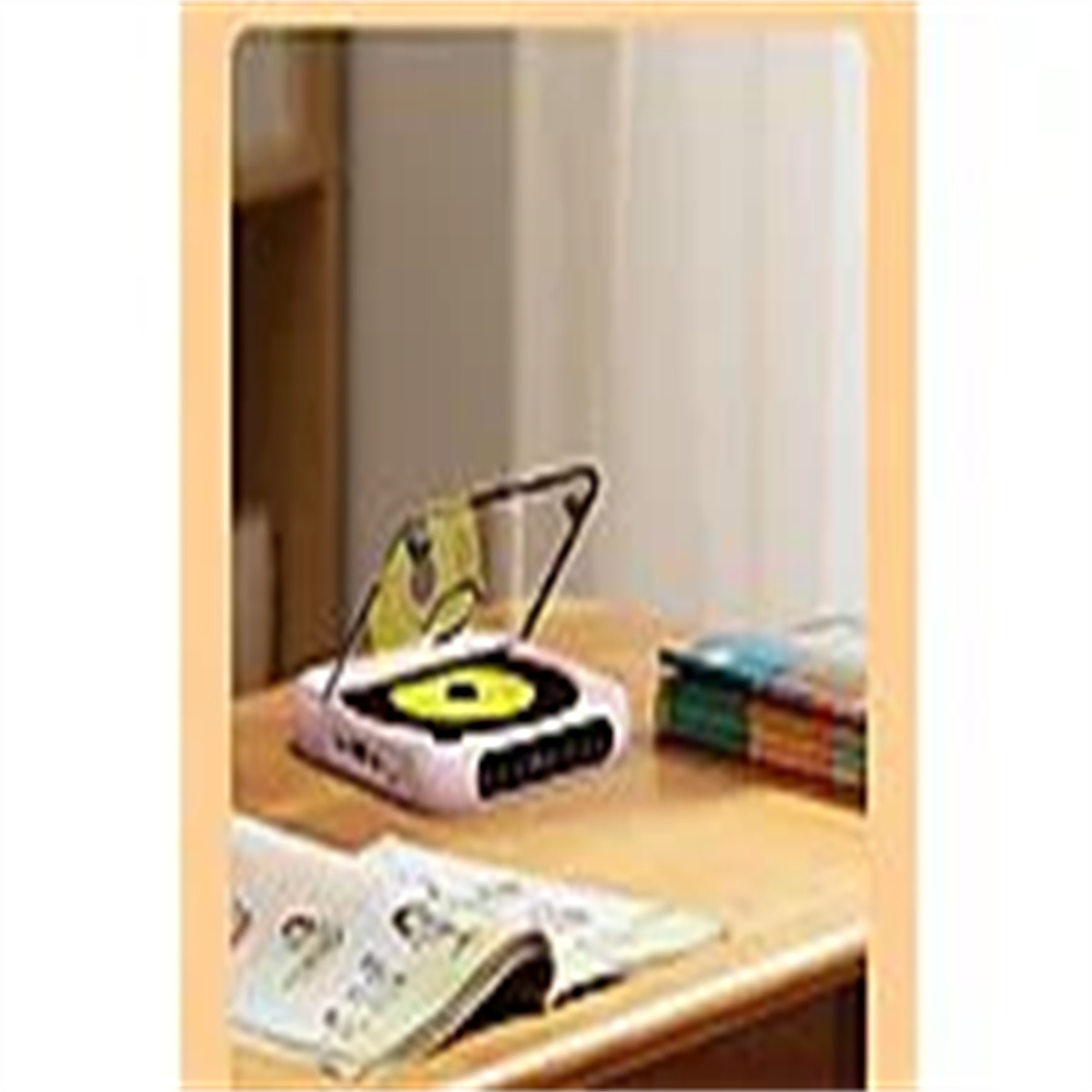Ein kleiner CD-Player auf einem Tisch mit einem Buch und CDs. Der Player ist rosa mit silbernem Scharnier.