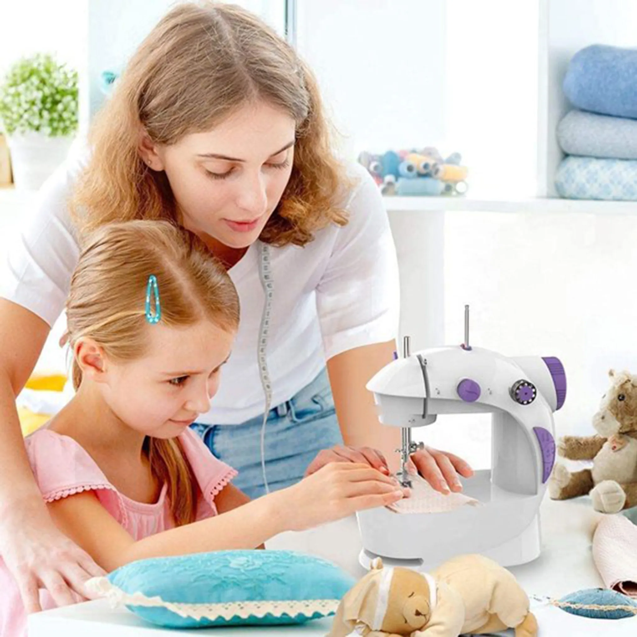 Eine Frau und ein Mädchen nähen mit einer weißen Nähmaschine. Ein blaues Kissen und ein Teddybär liegen auf dem Tisch.