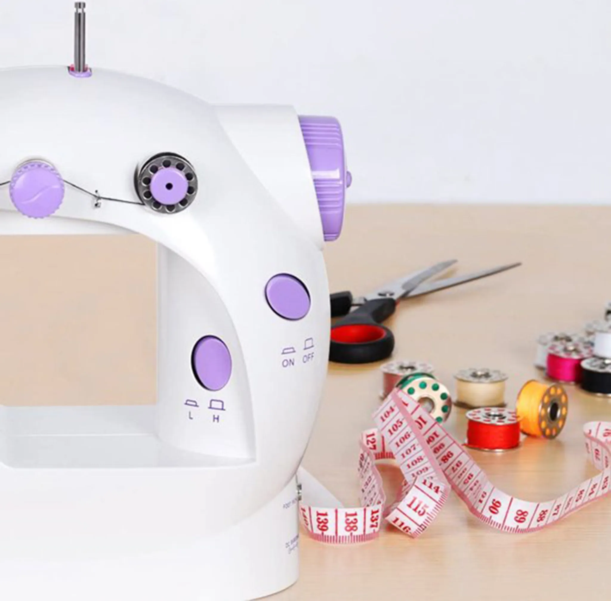 Weiße Nähmaschine, lila Akzente, Schere, Maßband und Garnrollen auf Holztisch.
