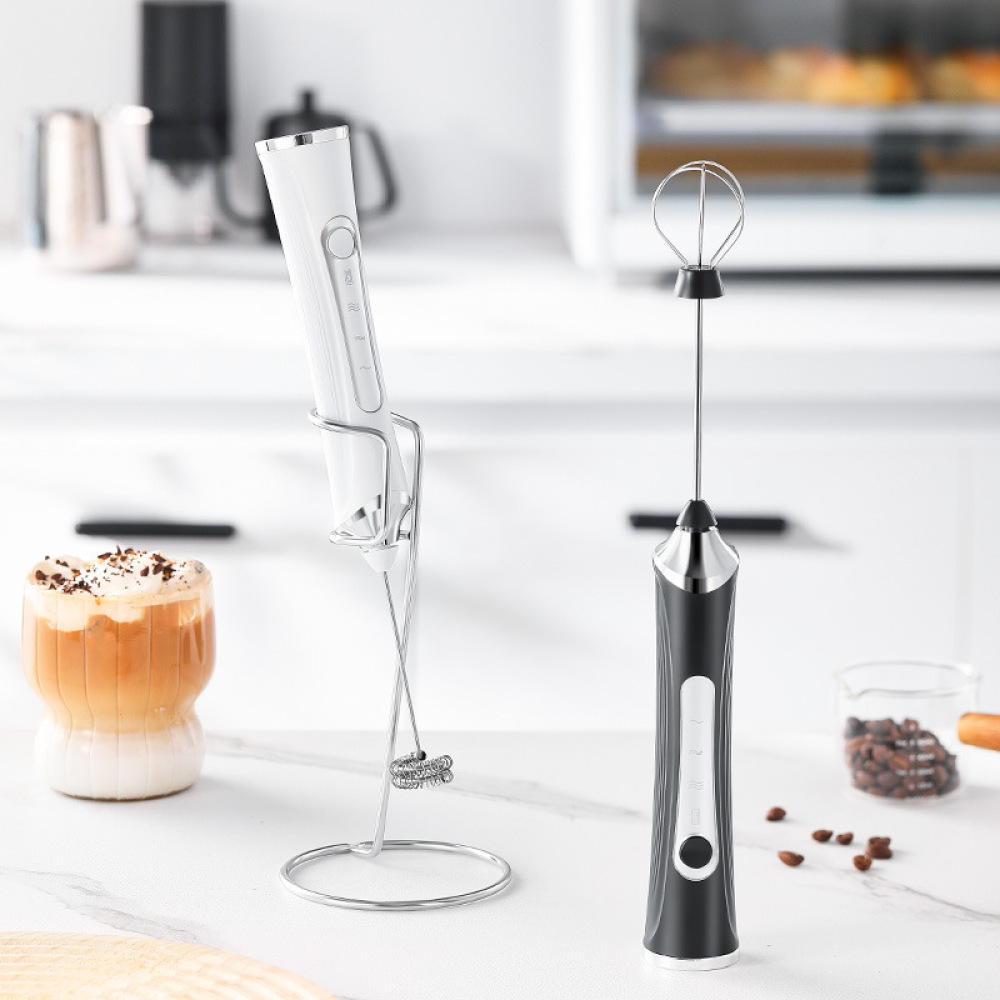 Zwei Mixer, einer schwarz und einer weiß, mit einem Latte in einem Glas und Kaffeebohnen auf der Theke.