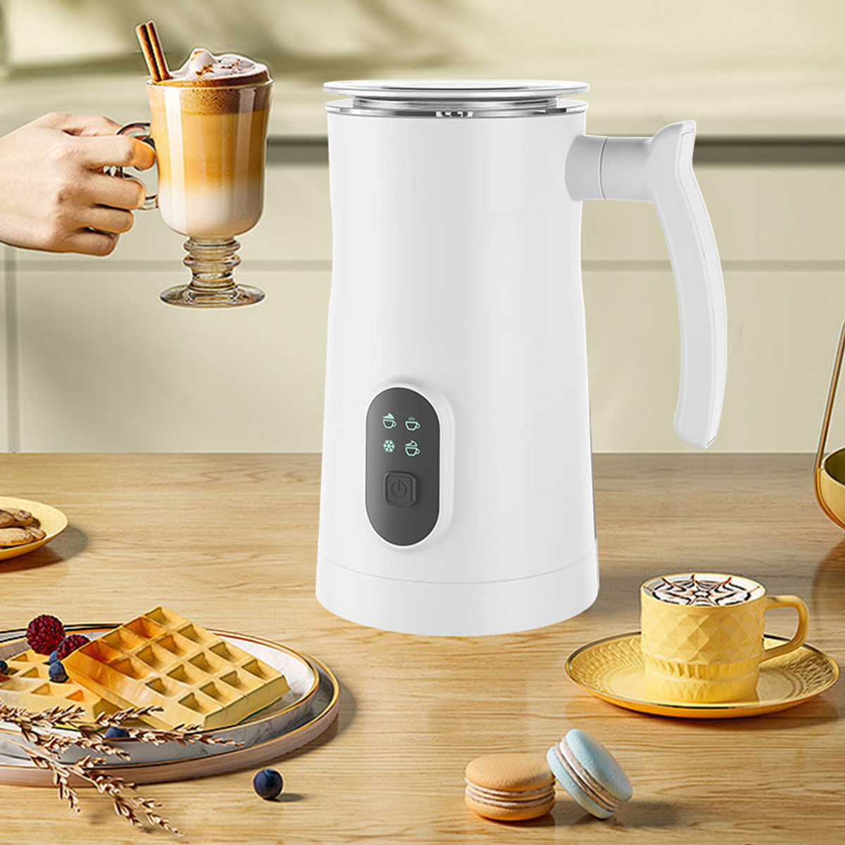 Ein weißer Milchaufschäumer mit Griff. Ein Latte und Waffel stehen auf dem Holztisch.